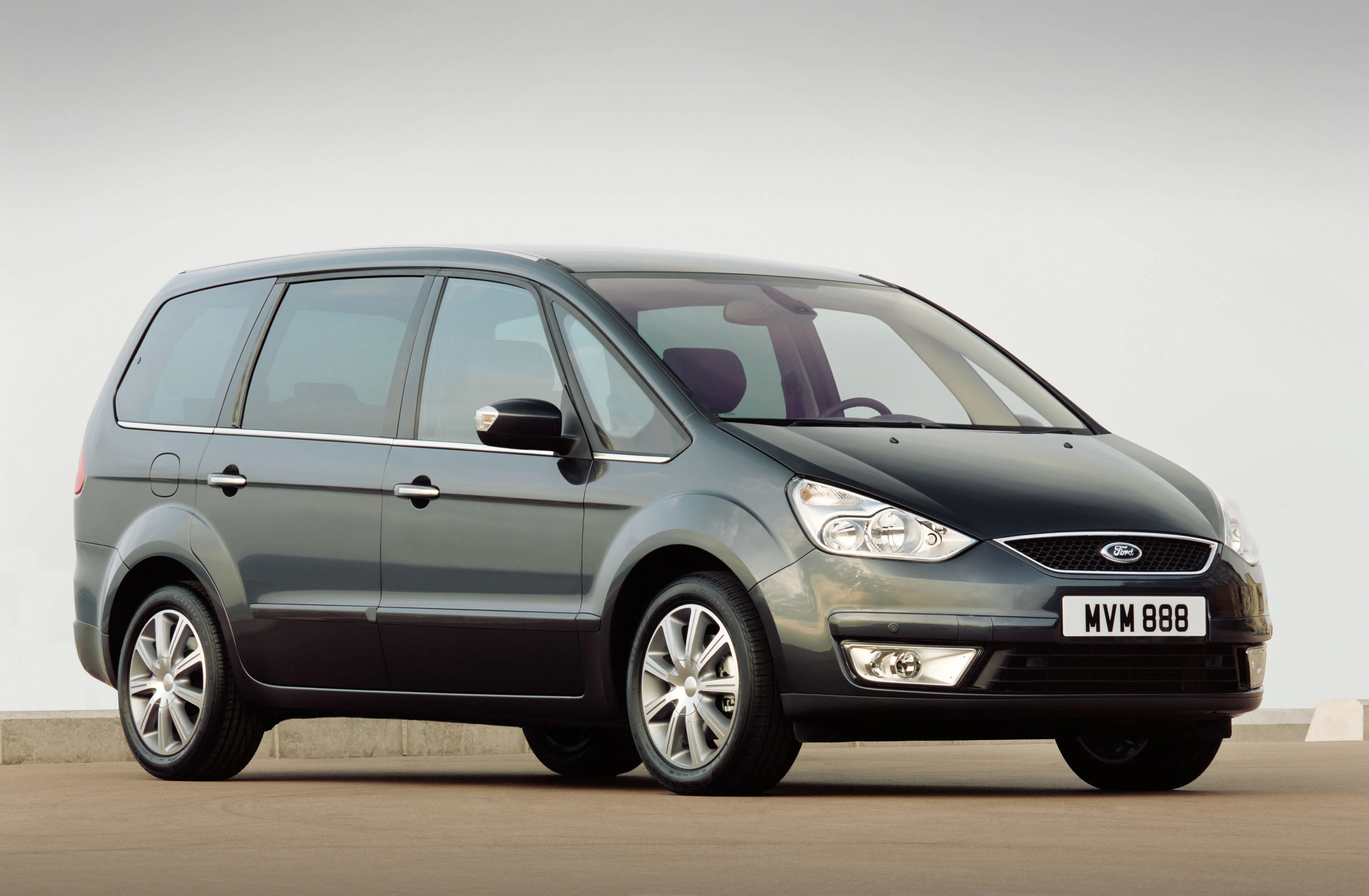 Dunkelgrauer Ford Galaxy Van geparkt auf Straße, seitliche Vorderansicht, klare Himmel im Hintergrund.