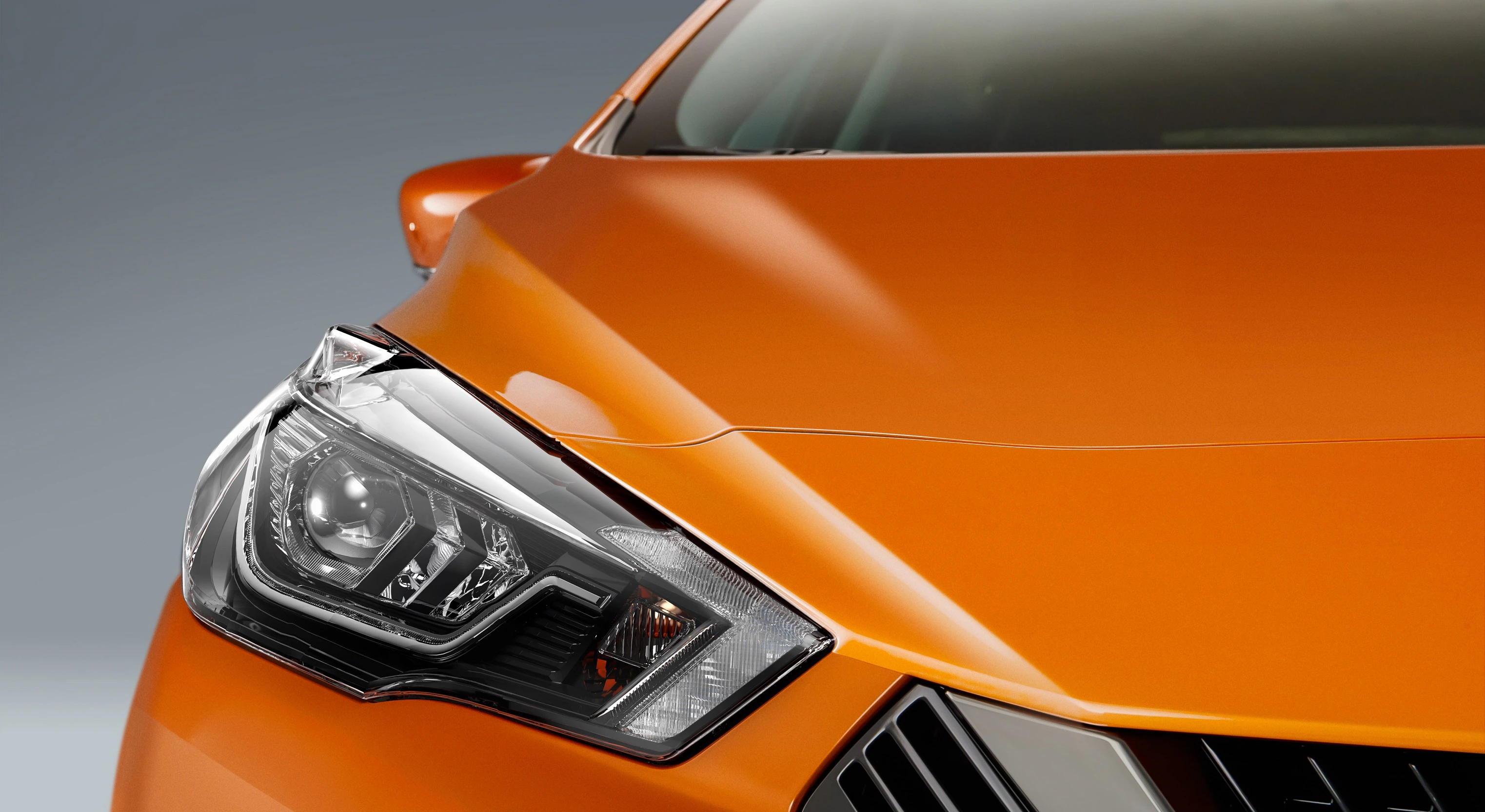 Nahaufnahme eines orangefarbenen Autos mit sichtbarem Scheinwerfer und einem Teil der Motorhaube; modernes Design.