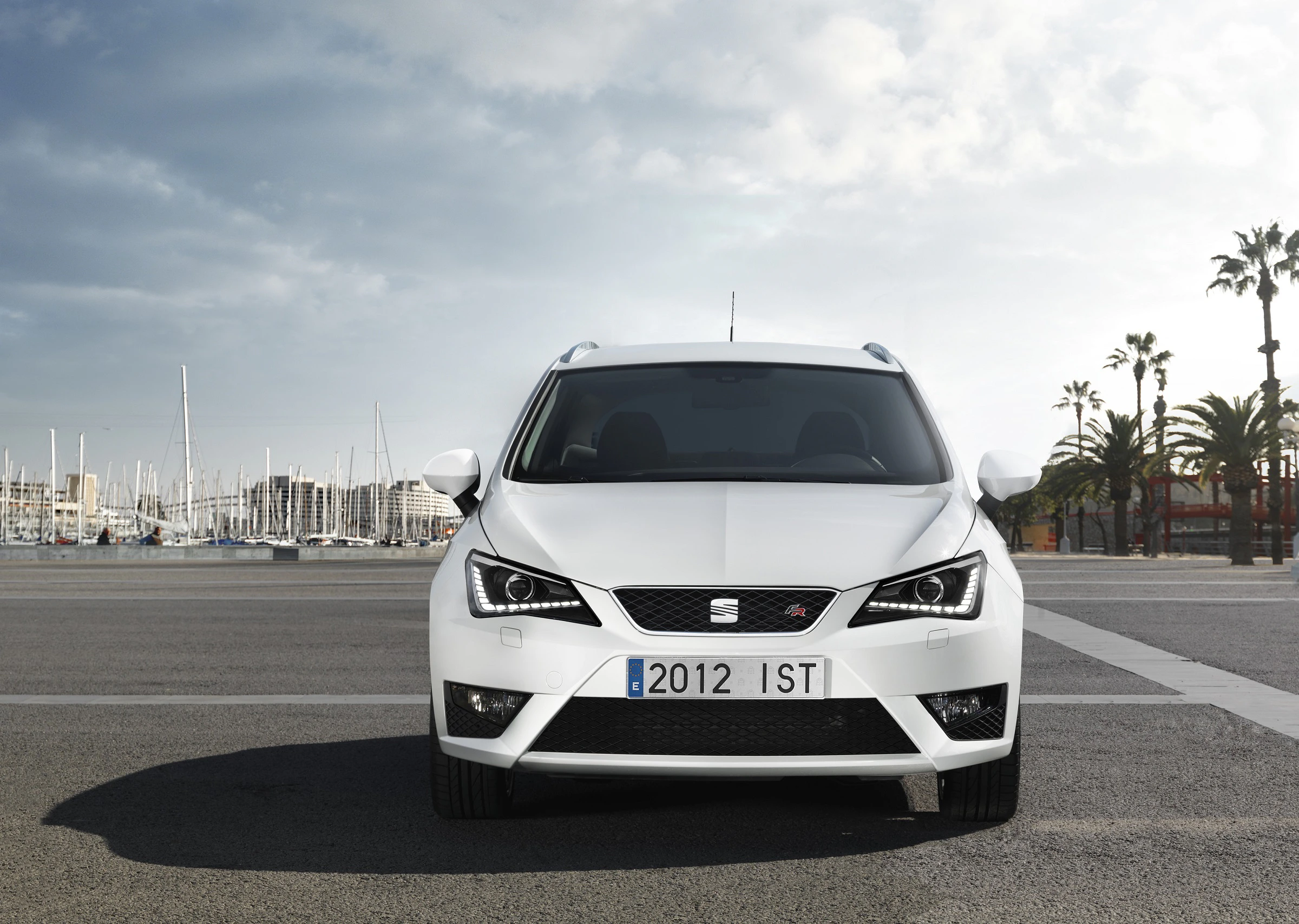 Ein weißer SEAT Ibiza auf einem Parkplatz am Hafen bei Tageslicht. Im Hintergrund Boote und Palmen.