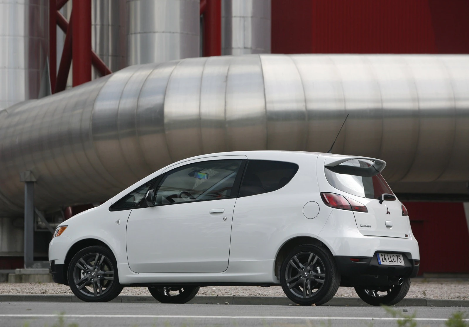 Weißes Auto, seitlich fotografiert, vor industriellem Hintergrund mit großen Metallröhren.