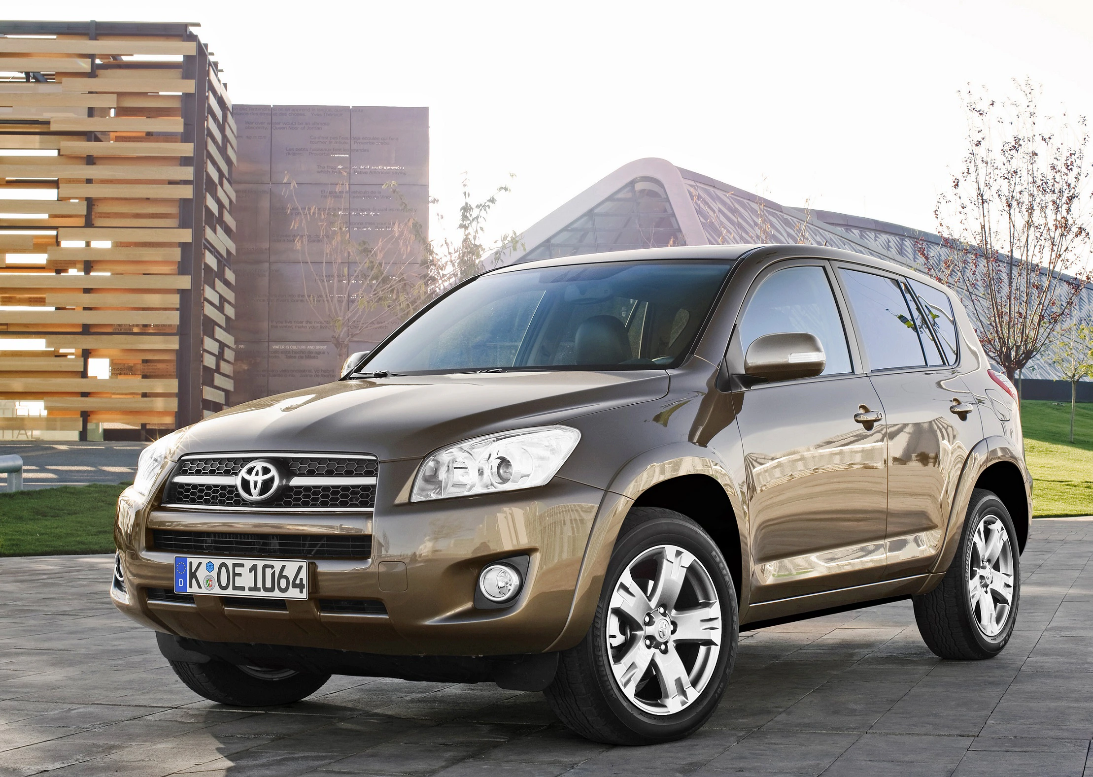 Brauner Toyota SUV steht draußen auf einem Pflasterweg, umgeben von modernen Gebäuden und dünnen Bäumen im Hintergrund.