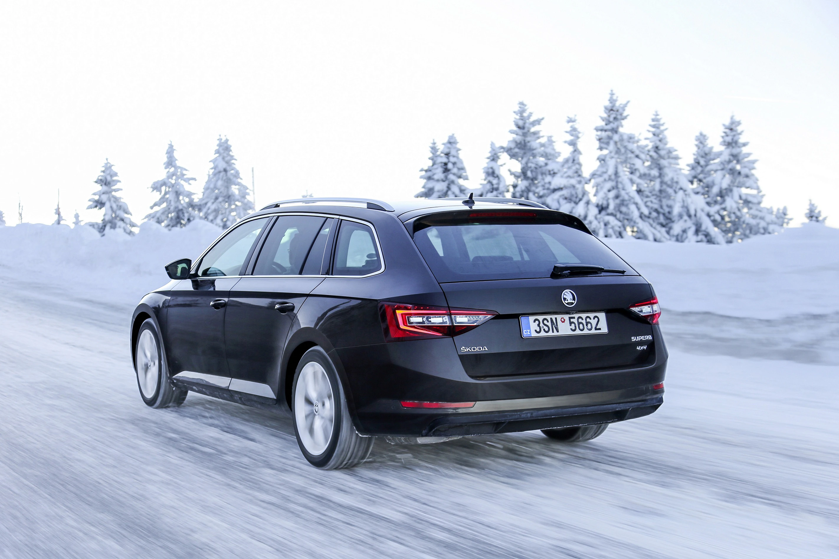 Schwarzer Skoda Kombi fährt auf schneebedeckter Straße, umgeben von schneebedeckten Bäumen, bei hellem, klarem Wetter.