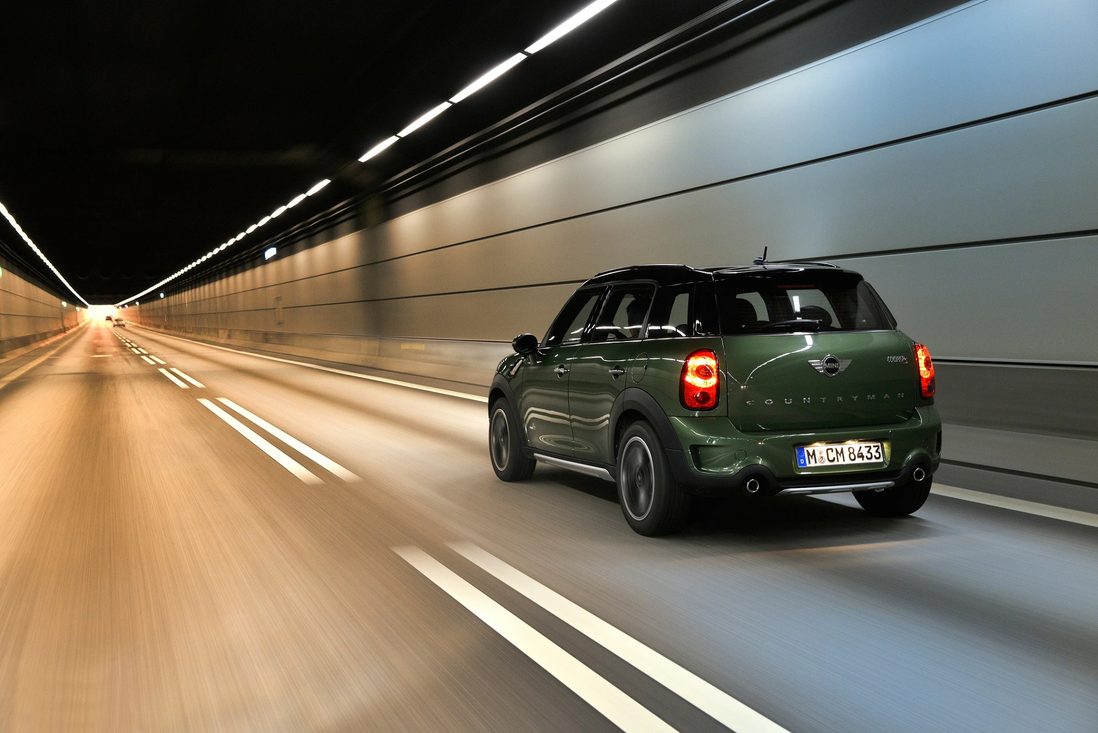 Grünes Auto fährt schnell durch einen beleuchteten Tunnel. Die Straße ist leer und die Lichter erzeugen Bewegungsunschärfe.