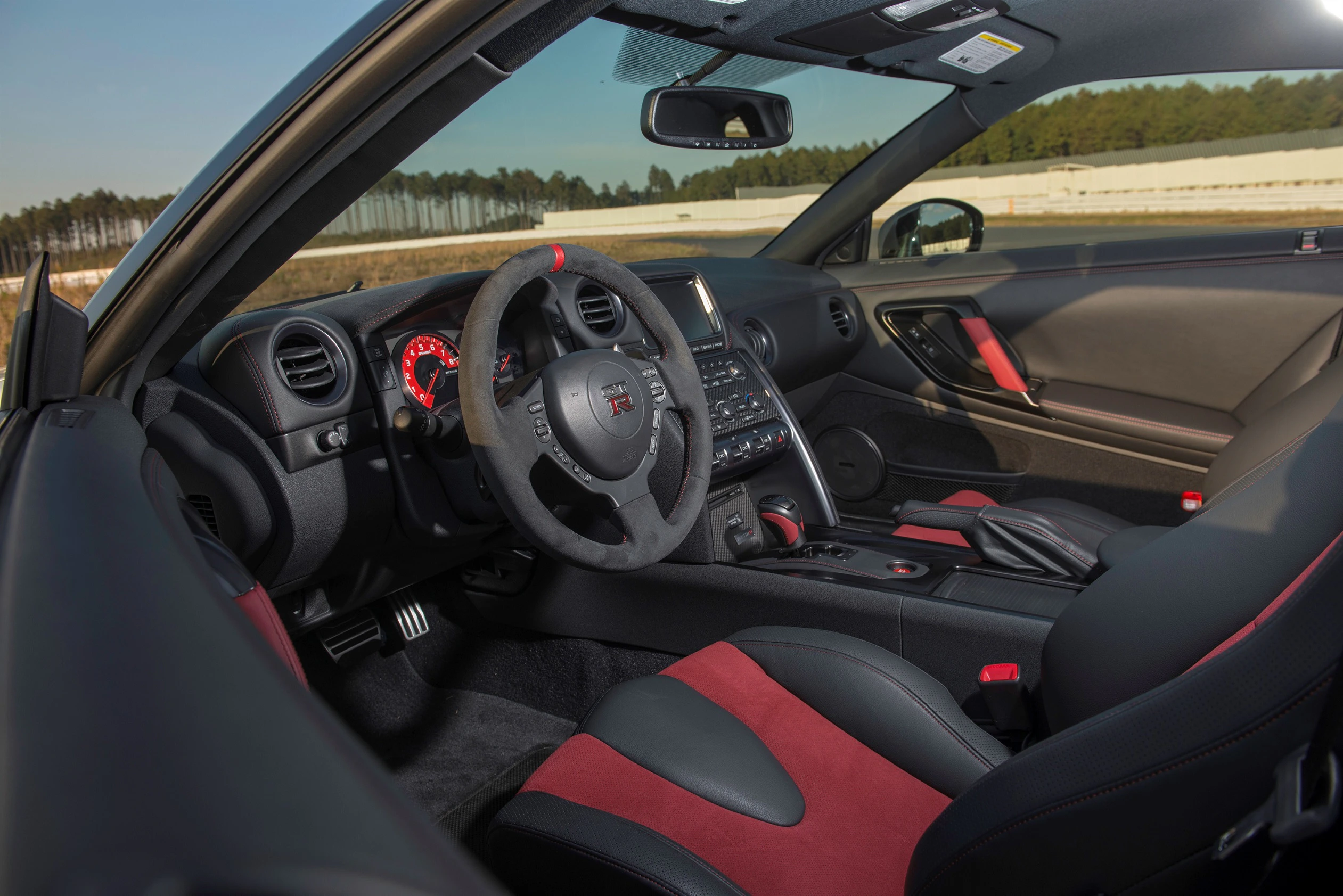 Innenraum eines sportlichen Autos mit schwarzem und rotem Interieur. Sicht auf das Lenkrad, Armaturenbrett und Schalensitze.