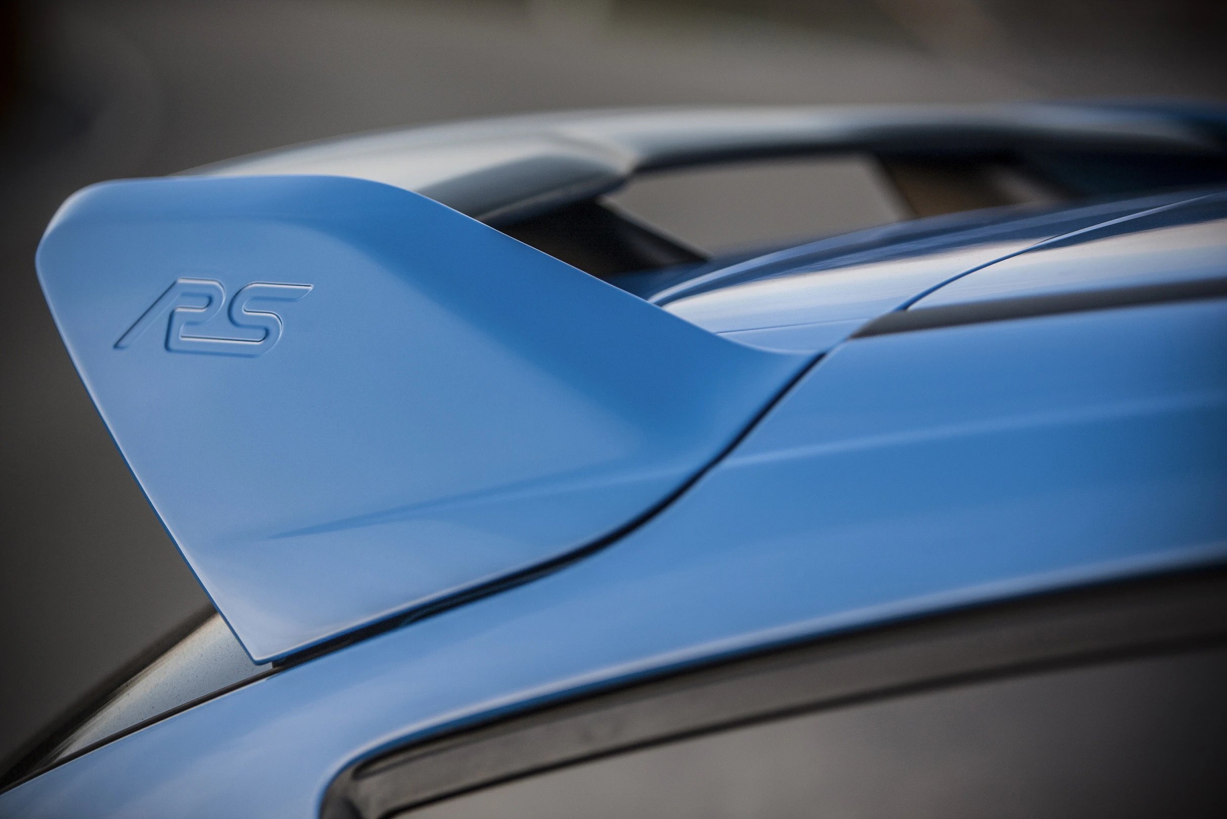 Blauer Heckspoiler eines Autos mit "RS"-Logo, aufgenommen in Nahaufnahme und bei Tageslicht.