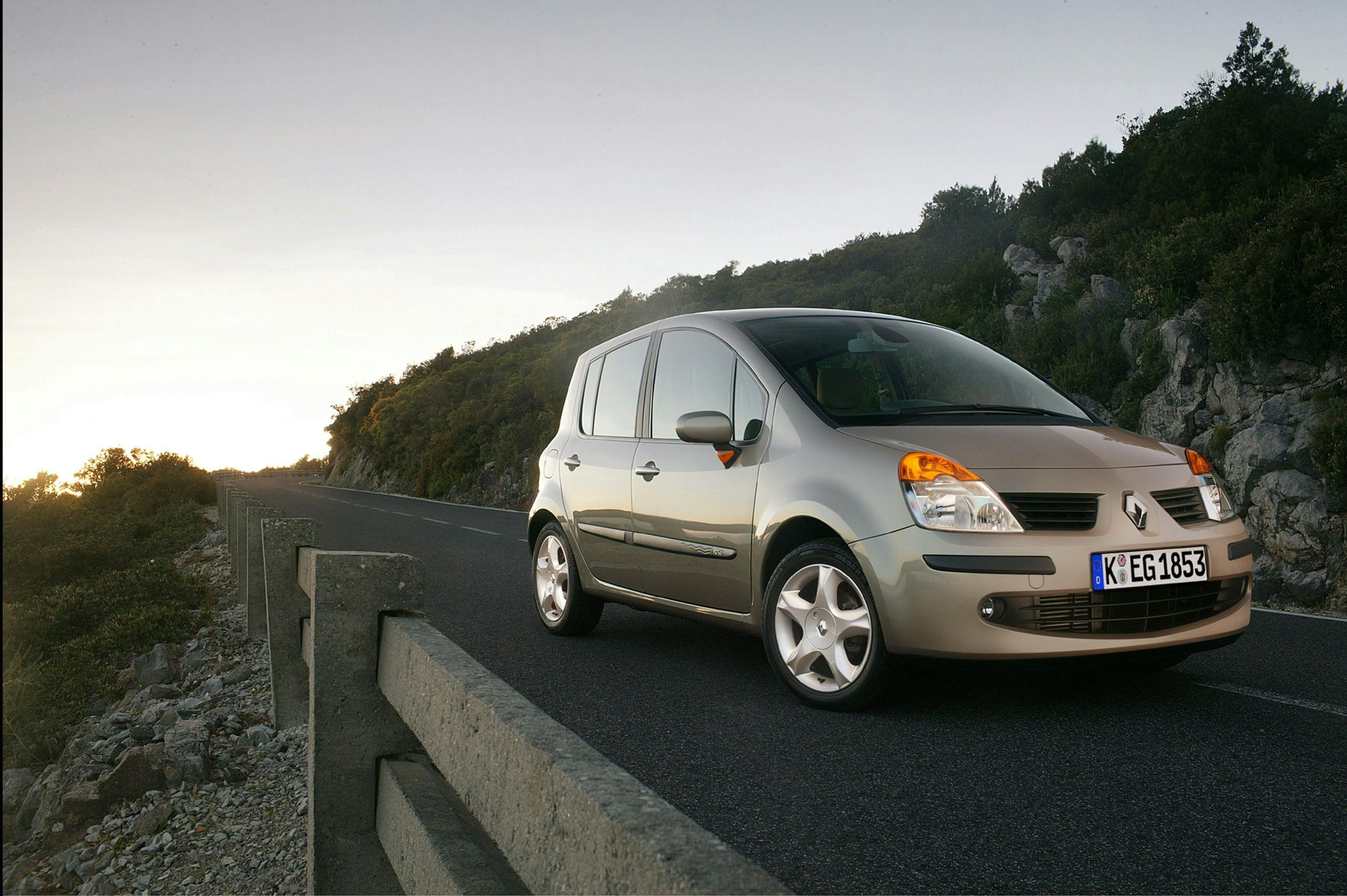 Beiger Renault Modus auf asphaltierter Bergstraße bei Sonnenuntergang, umgeben von Felsen und Bäumen.