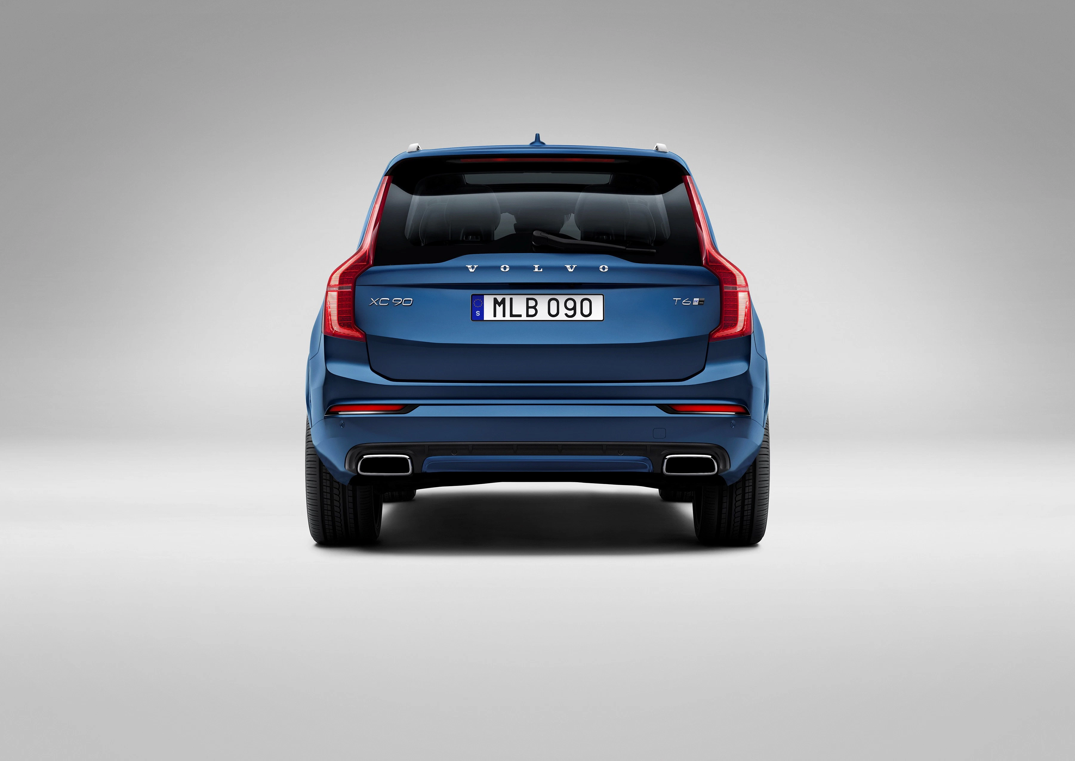 Rückansicht eines blauen Volvo XC90 SUV vor grauem Hintergrund, mit sichtbarem Emblem, Modellbezeichnung und Auspuffrohren.
