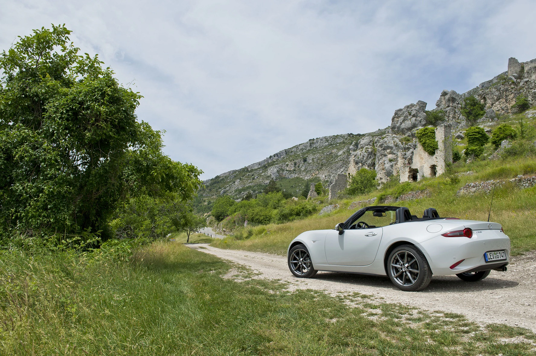 Weißes Cabrio auf einem ländlichen Weg, umgeben von grünen Wiesen und Felsen unter blauem Himmel.