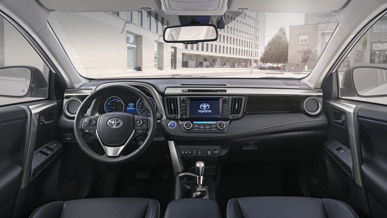 Innenraum eines Autos mit Lenkrad, Armaturenbrett und Touchscreen. Moderne Ausstattung, Blick auf Gebäude durch die Windschutzscheibe.