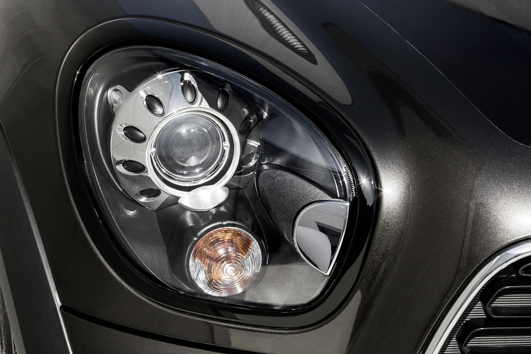 Nahaufnahme eines Autoscheinwerfers mit modernem Design und verchromten Details an einem dunkelgrauen Fahrzeug.