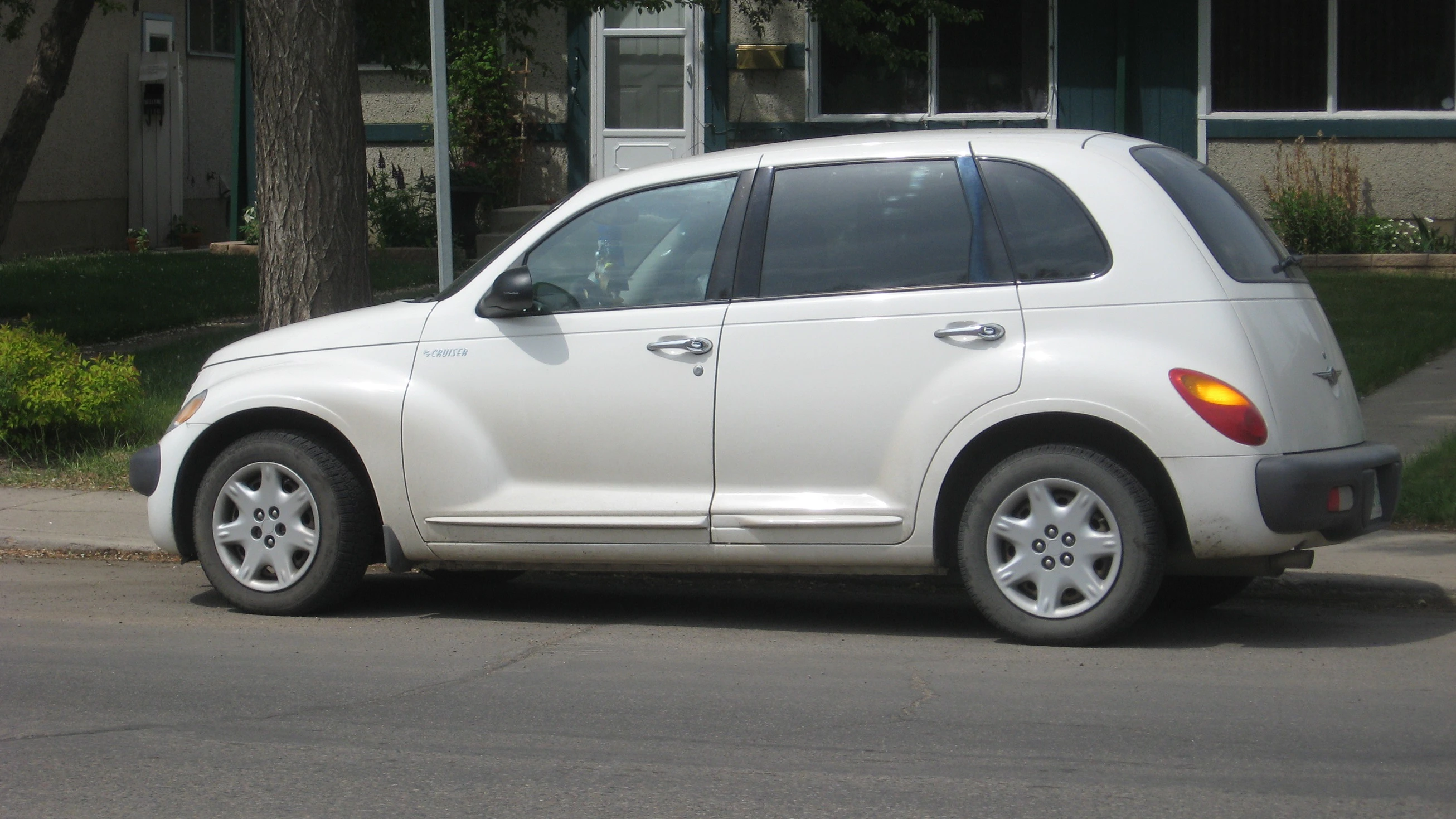 Weißer Chrysler PT Cruiser geparkt am Straßenrand vor einem Wohngebäude.