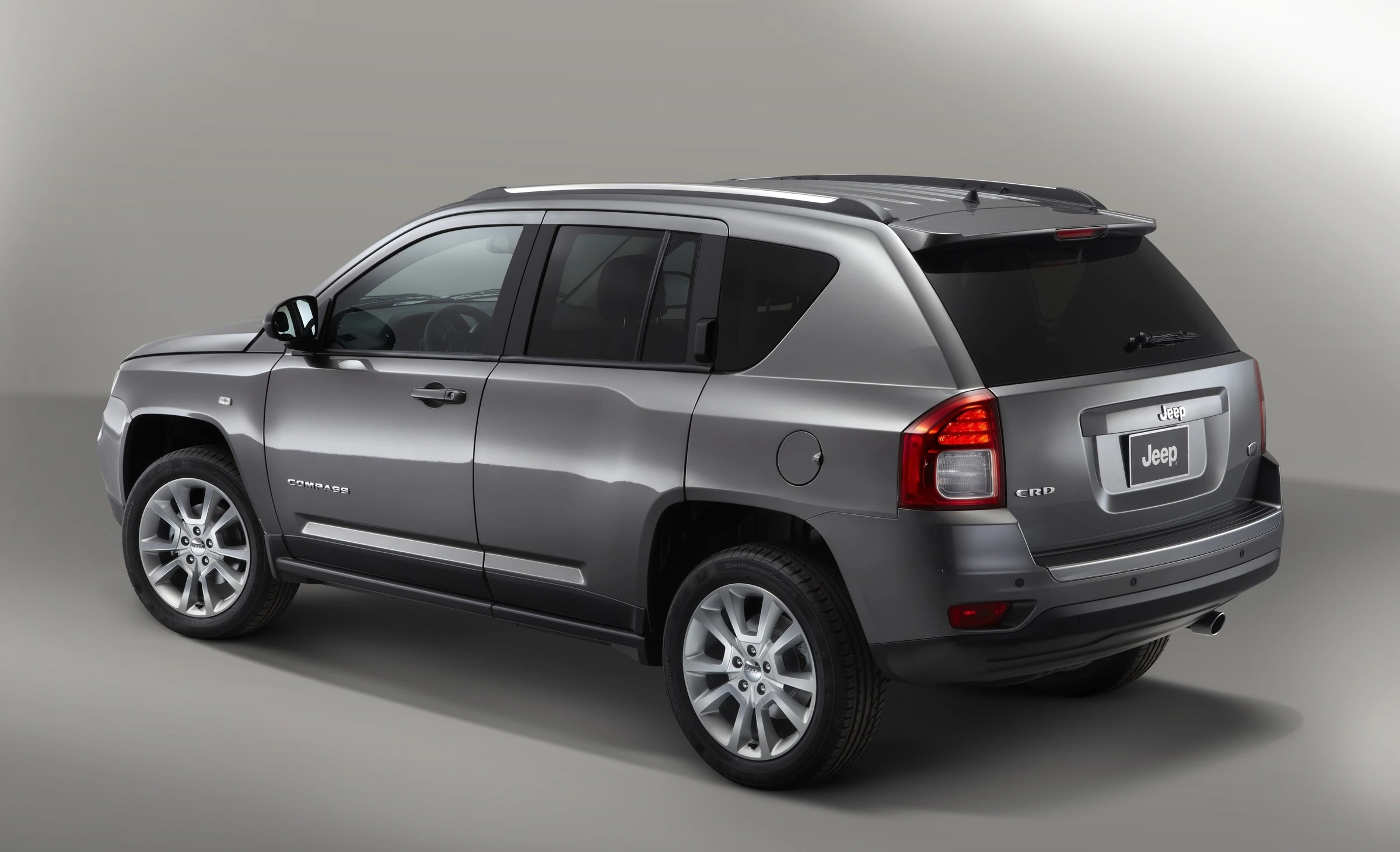 Grauer Jeep Compass SUV, Seitenansicht, steht in einem Studio vor neutralem Hintergrund. Fahrzeug hebt sich durch klare Linien und modernes Design hervor.