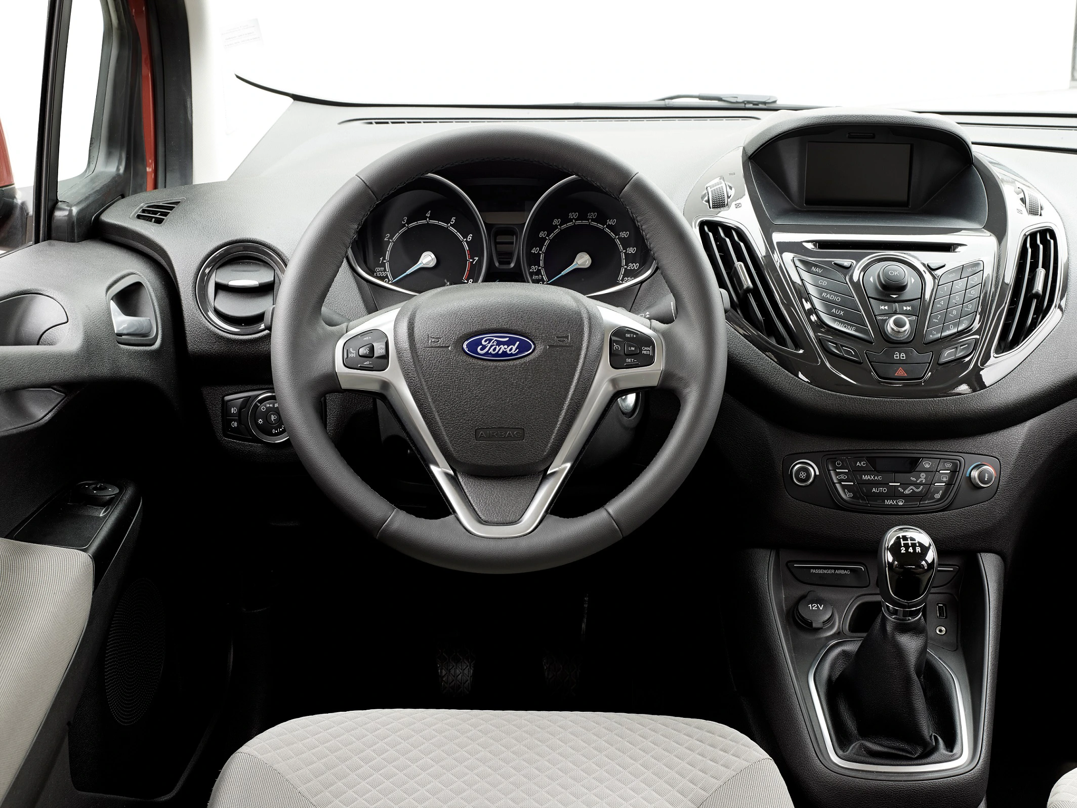 Innenraum eines Ford-Autos mit Lenkrad, Armaturenbrett und Schalthebel. Sicht auf Tacho und Bedienelemente. Beige Polsterung.