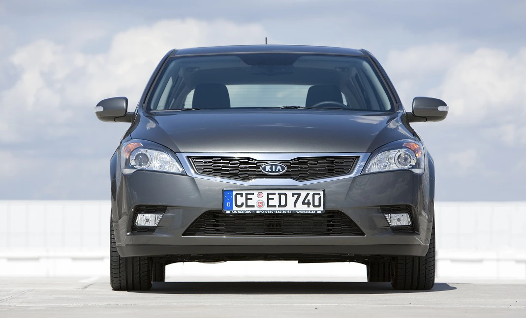Ein grauer Kia Ceed steht auf einem Parkplatz vor einem blauen Himmel mit Wolken, frontal fotografiert.