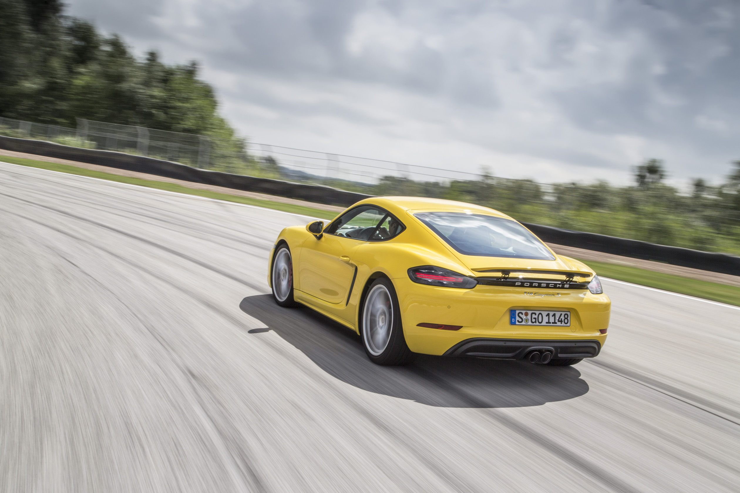 Gelber Sportwagen fährt schnell auf Rennstrecke bei bewölktem Himmel, sichtbar von hinten, leicht nach links geneigt.
