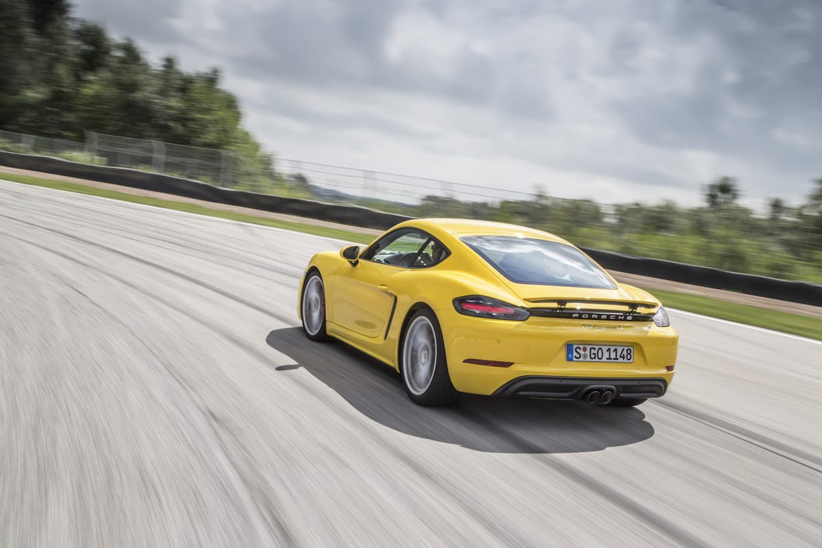 Gelber Sportwagen fährt schnell auf Rennstrecke bei bewölktem Himmel, sichtbar von hinten, leicht nach links geneigt.