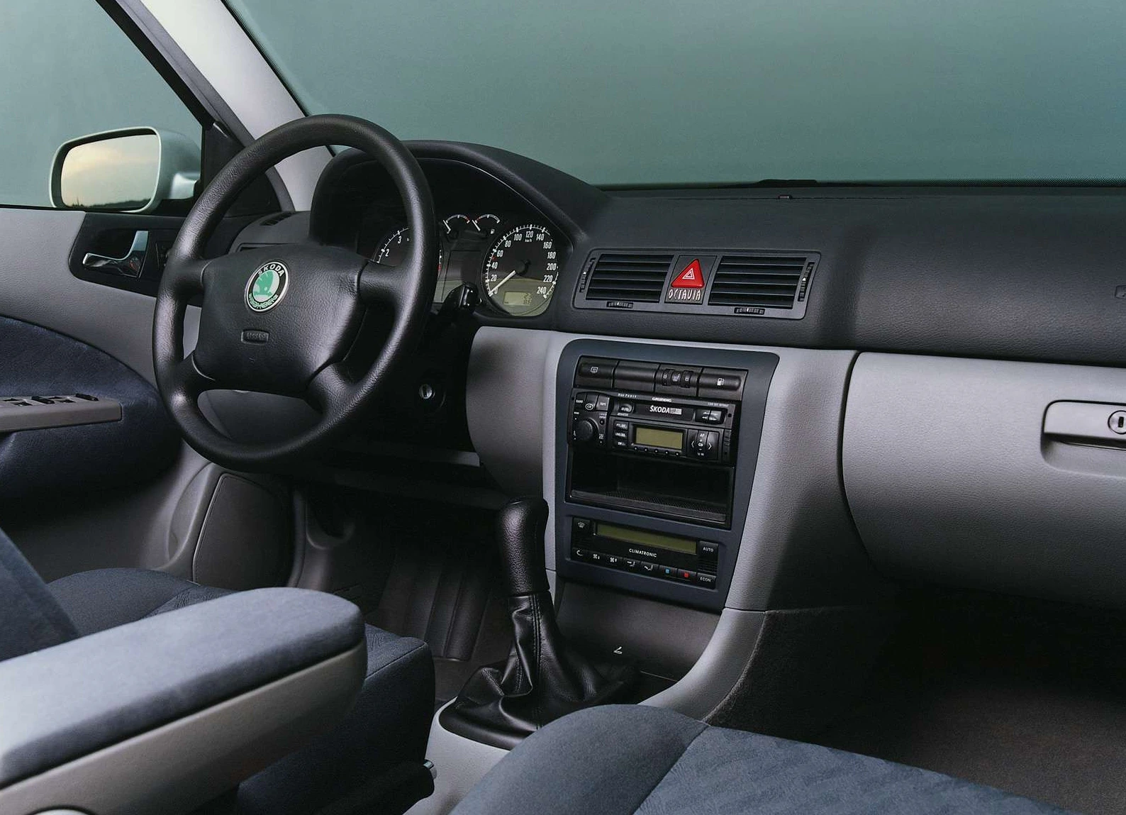 Innenraum eines Autos mit schwarzem Armaturenbrett, Lenkrad, Schalthebel und Tacho. Zentrales Bedienfeld mit Klimaanlage und Radio.