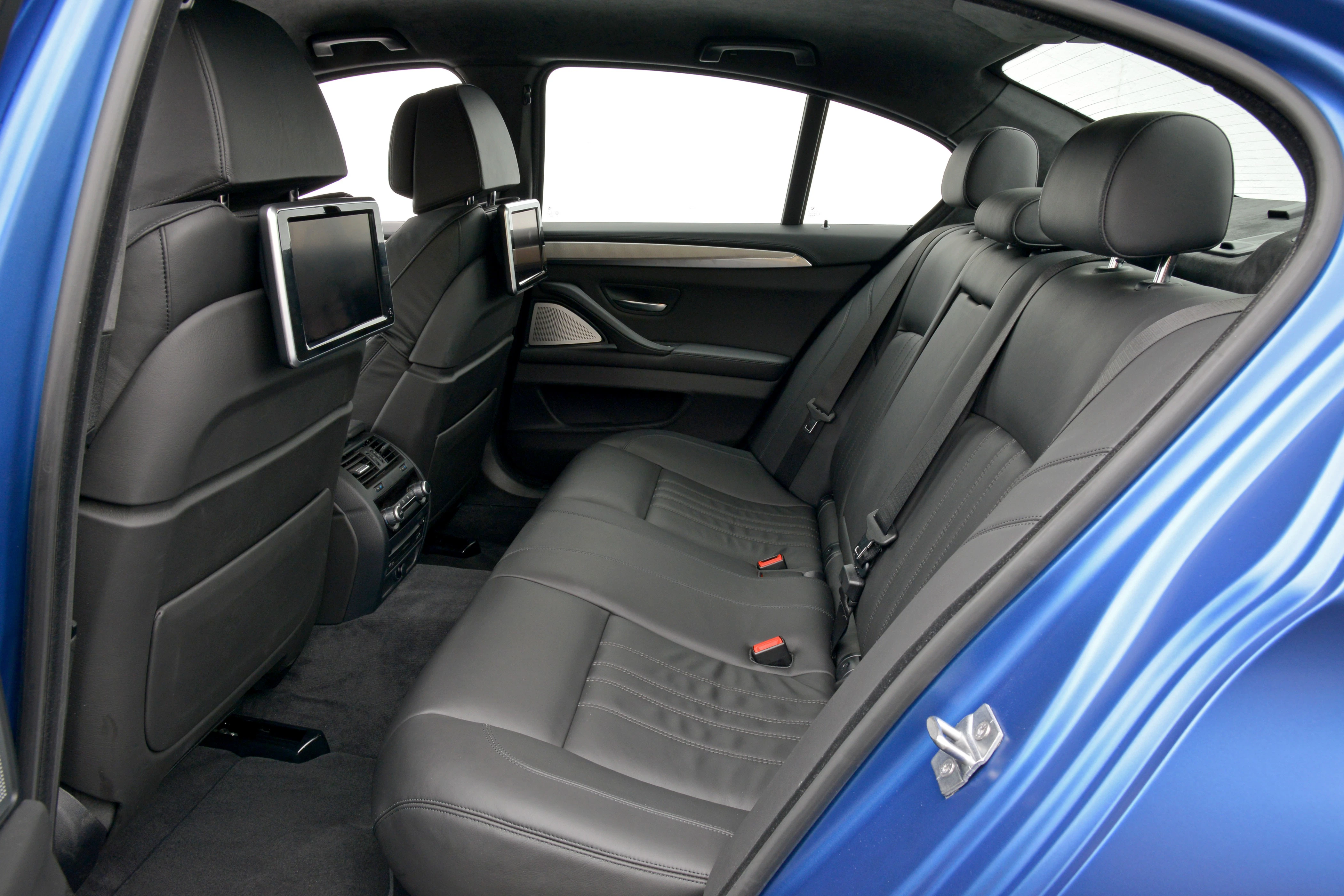 Innenraum eines blauen Autos, Rücksitz mit schwarzem Leder, zwei Bildschirme an den Kopfstützen, moderne Ausstattung.