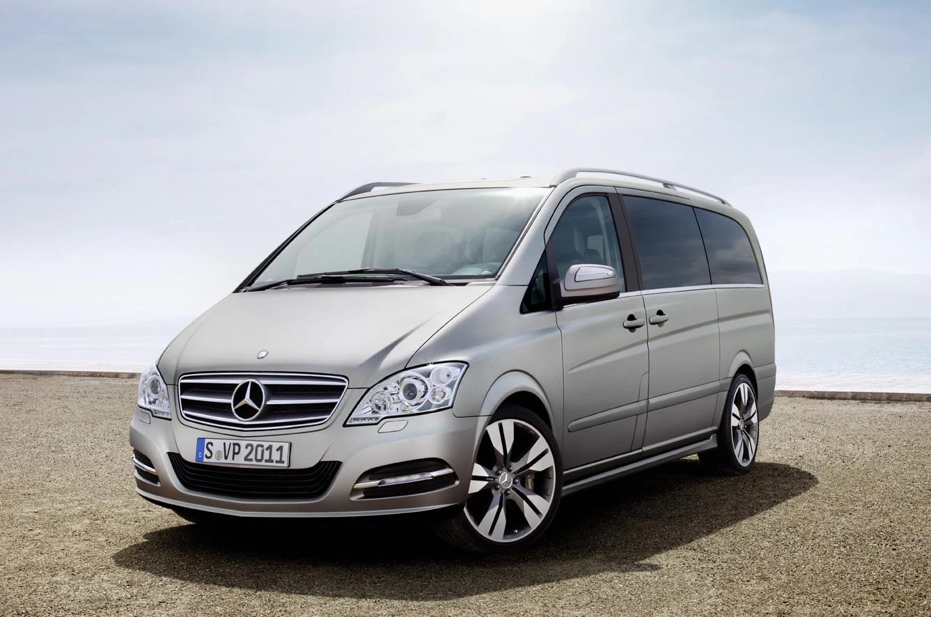 Silberner Mercedes-Benz Viano auf einem leeren Parkplatz vor einem nebligen Hintergrund, linksparkend, mit erkennbaren Markenzeichen und Autokennzeichen.