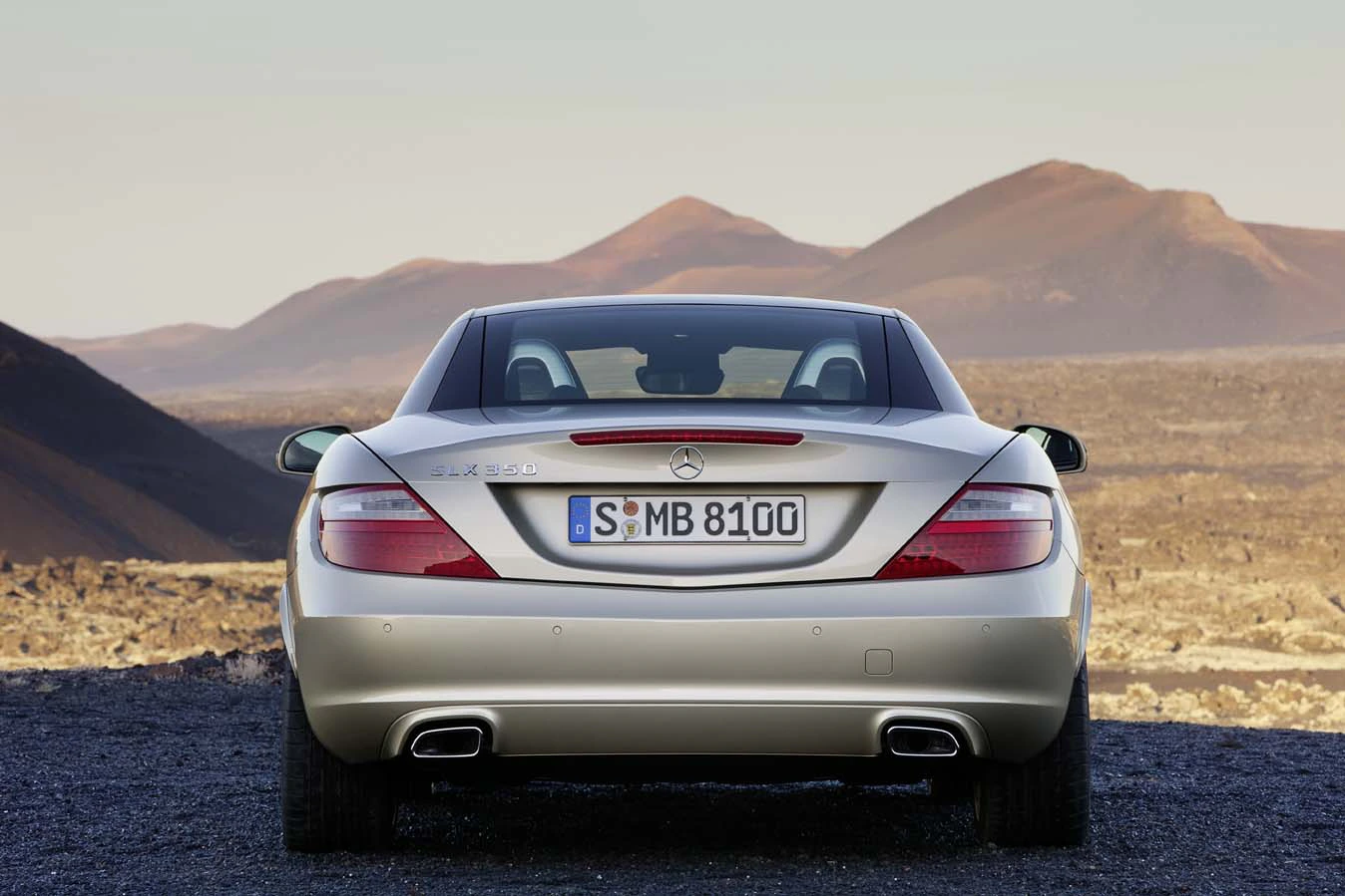 Silberner Mercedes-Benz SLK 55 AMG steht in einer wüstenartigen Landschaft, Heckansicht mit nummerierten Kennzeichen, umgeben von Hügeln.