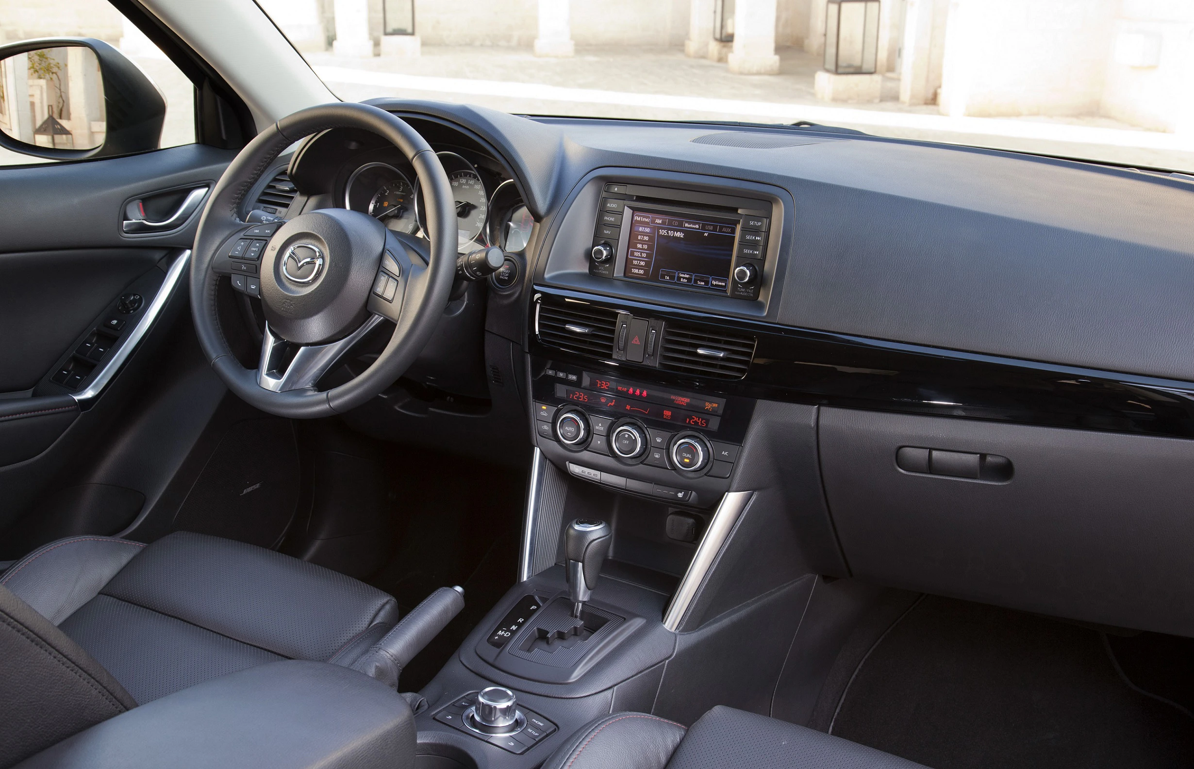 Innenraum eines Autos mit grauer Polsterung, moderne Armaturen, Zentraldisplay, Lenkrad links und Automatikschaltung zu sehen.