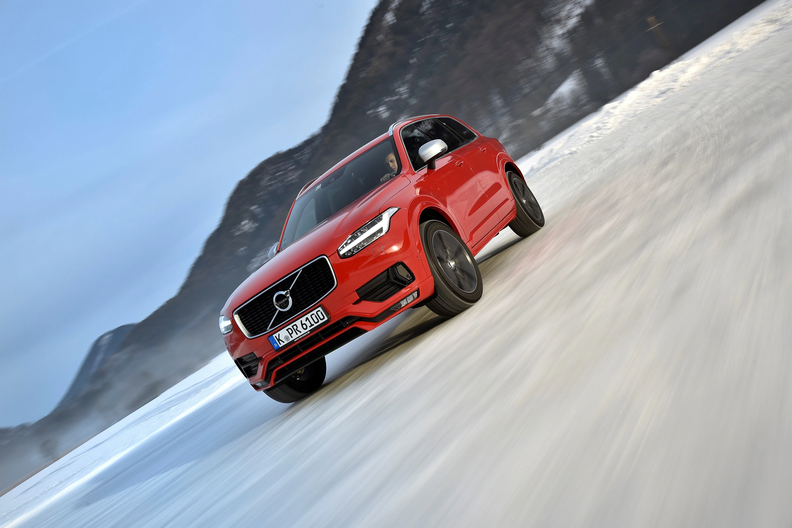 Roter SUV fährt dynamisch auf schneebedeckter Straße in bergiger Landschaft, mit unscharfem Hintergrund für Bewegungseffekt.