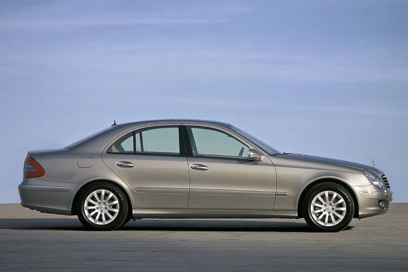 Silberner Mercedes-Benz Limousine in Seitenansicht auf asphaltierter Fläche vor blauem Himmel.