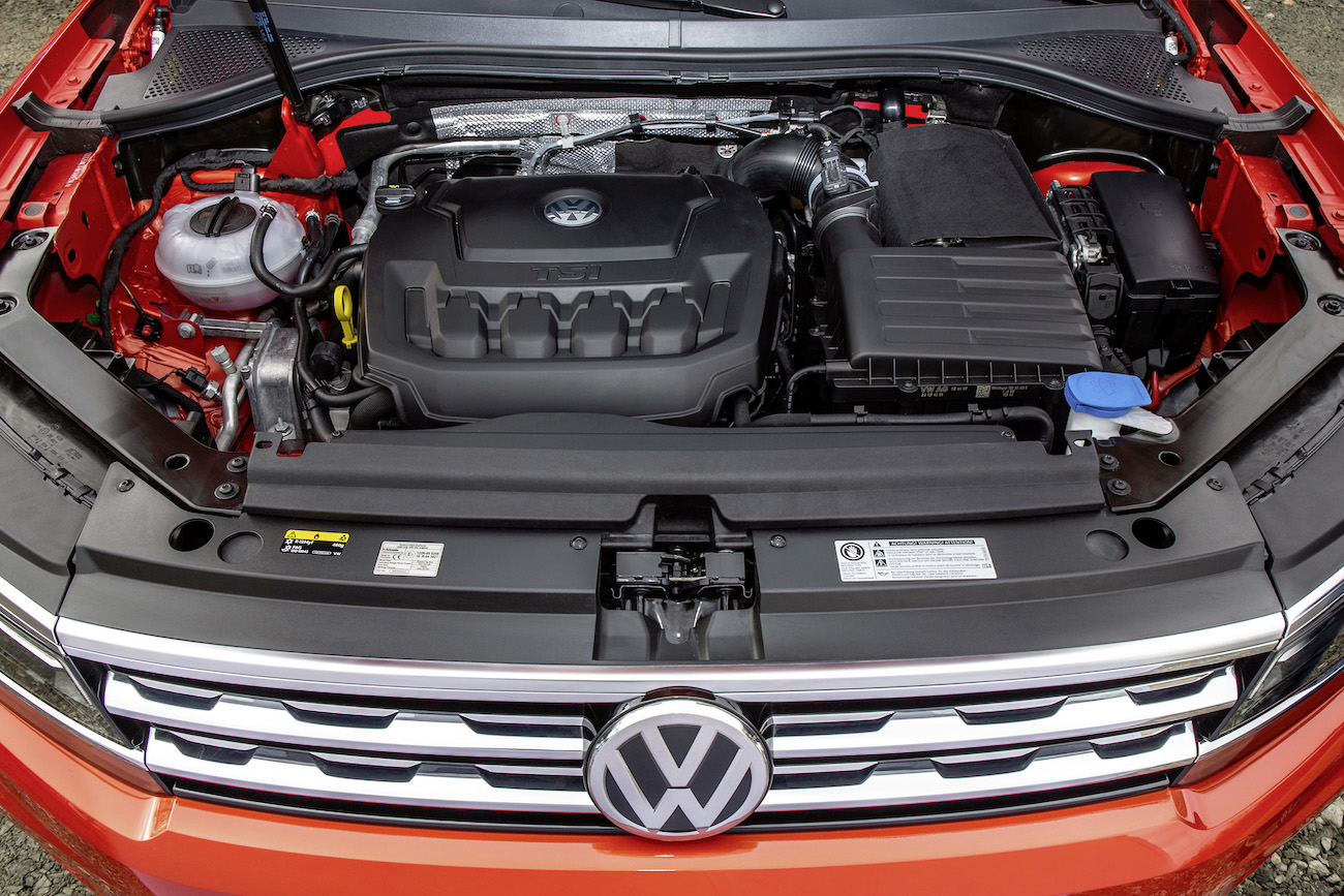 Motorraum eines roten VW-Autos mit sichtbarem VW-Logo auf dem Kühlergrill. Der Motor und Teile des Kühlsystems sind erkennbar.