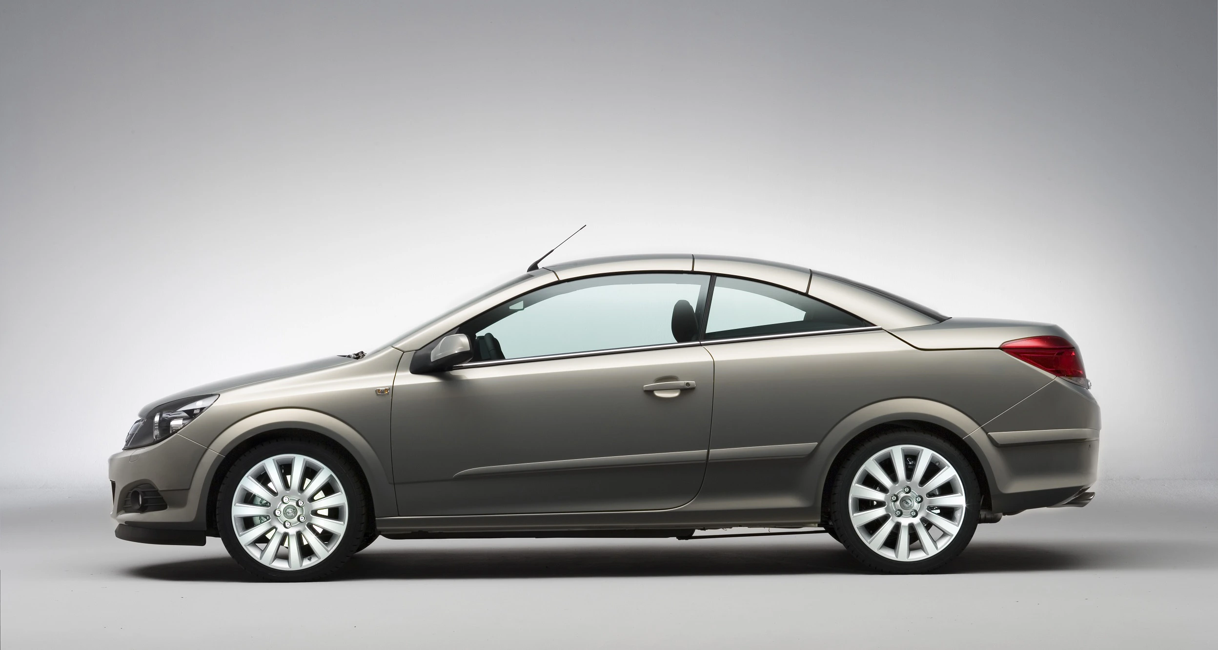 Silbernes Coupé-Auto seitlich vor grauem Hintergrund, mit sportlicher Karosserie und modernen Felgen.