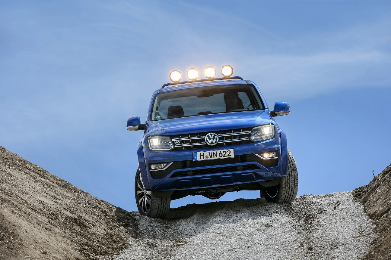 Blauer Geländewagen von Volkswagen fährt einen Hügel hinunter, mit leuchtenden Scheinwerfern und staubiger Umgebung unter blauem Himmel.