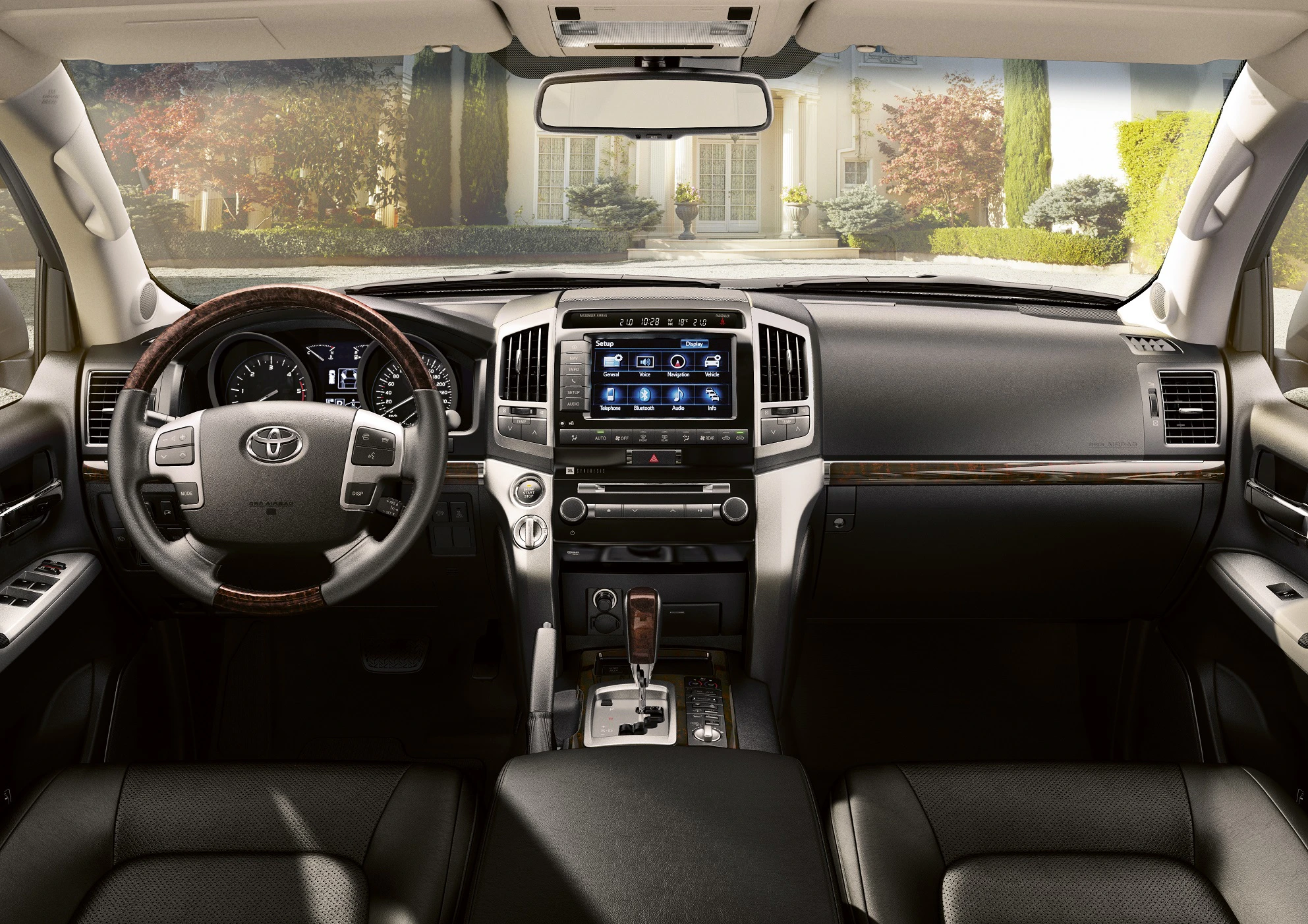 Innenansicht eines luxuriösen Auto-Cockpits mit Lederlenkrad, Touchscreen und modernen Armaturen. Außenausblick auf gepflegten Garten.