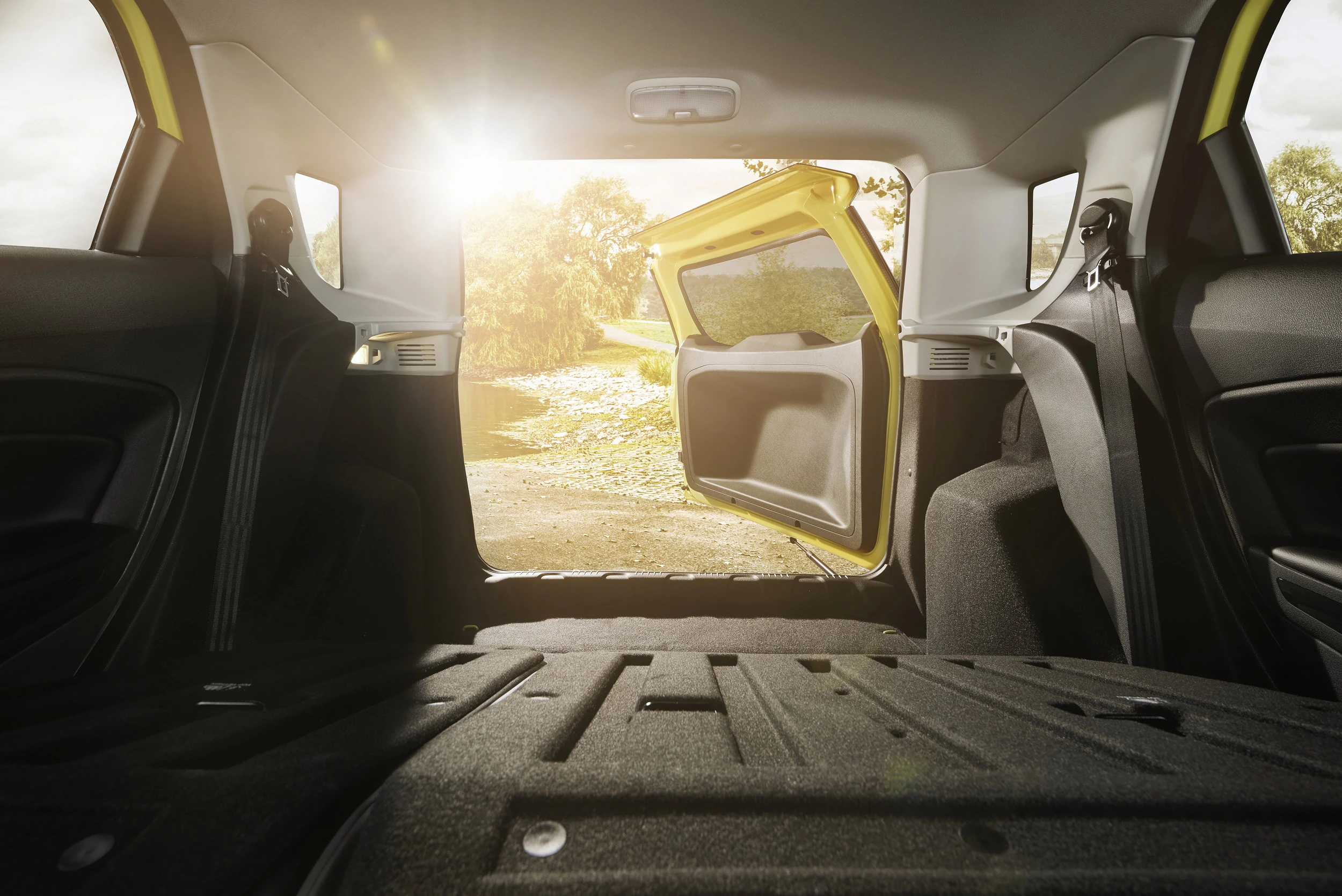Rückansicht eines Autos mit geöffneter Kofferraumklappe, durch die Sonnenlicht hereinfällt. Innenraum mit umgeklappter Rückbank.