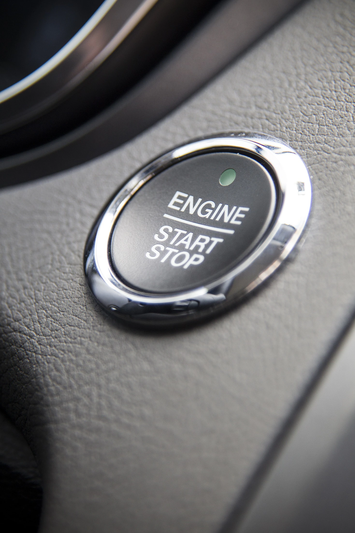 Nahaufnahme eines runden Start-Stopp-Knopfs in einem Auto, umgeben von einer silbernen Umrandung auf grauem Armaturenbrett.