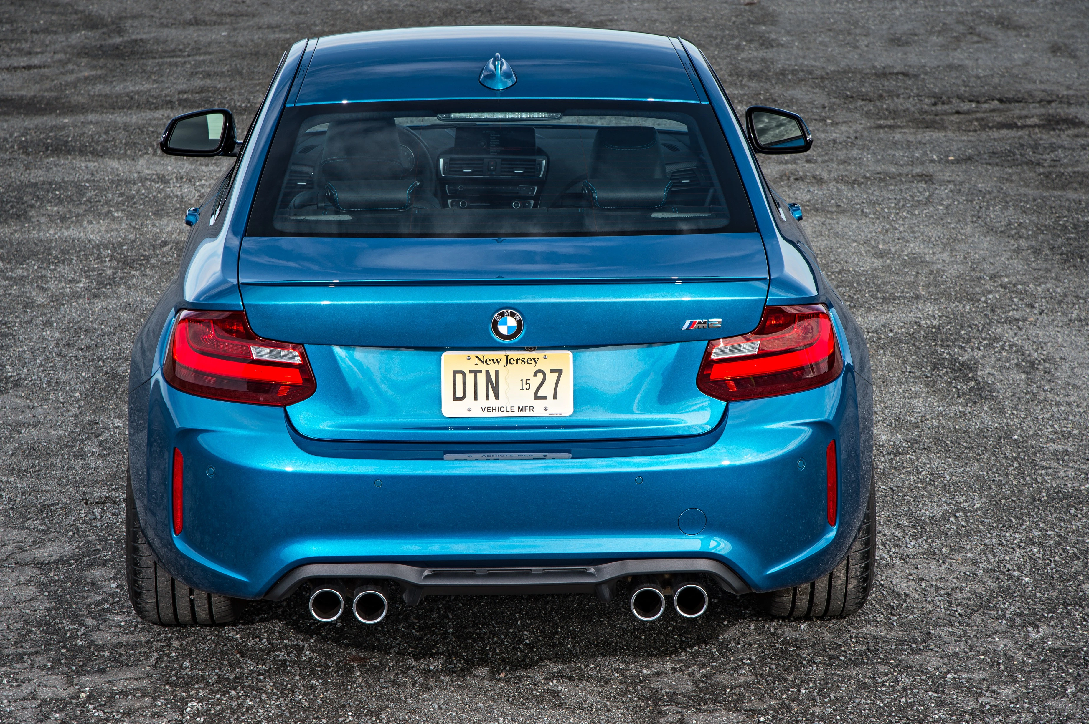 Blauer BMW M2 von hinten, geparkt auf grauem Asphalt, mit doppeltem Auspuff und New Jersey-Kennzeichen.