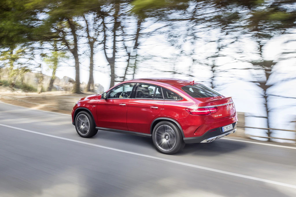 Roter SUV fährt dynamisch eine Landstraße entlang, im Hintergrund Bäume und ein unscharfer Himmel.
