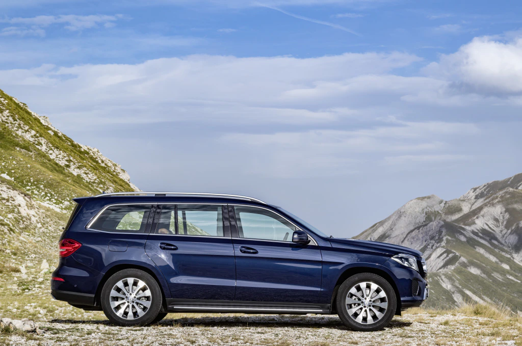 Dunkelblauer SUV parkt in einer bergigen Landschaft unter blauem Himmel mit vereinzelten Wolken.
