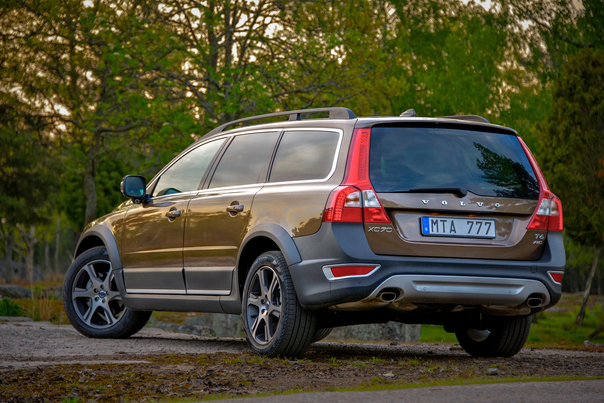 Brauner Volvo XC70 T6 SUV auf einer Kiesstraße, umgeben von Bäumen, von hinten rechts gesehen. Nummernschild: MTA 777.