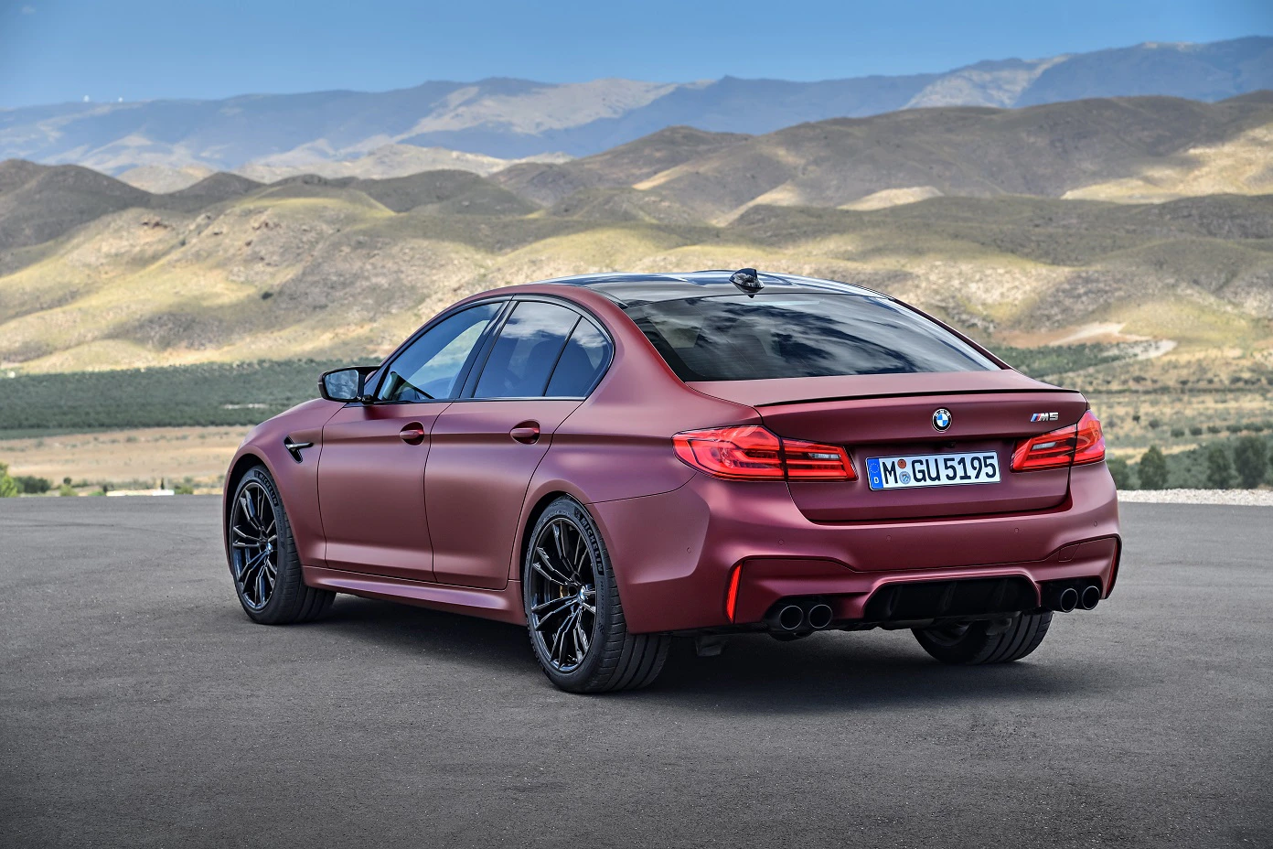 Roter BMW M5 auf einer Straße vor bergiger Landschaft, mit sportlichem Design und robusten Reifen.