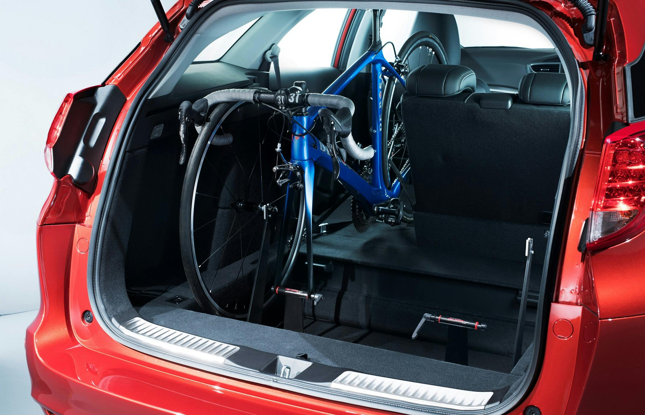 Rotes Auto, in dessen Kofferraum ein blaues Rennrad verstaut ist. Die Rücksitze sind umgeklappt, um Platz für das Fahrrad zu schaffen.