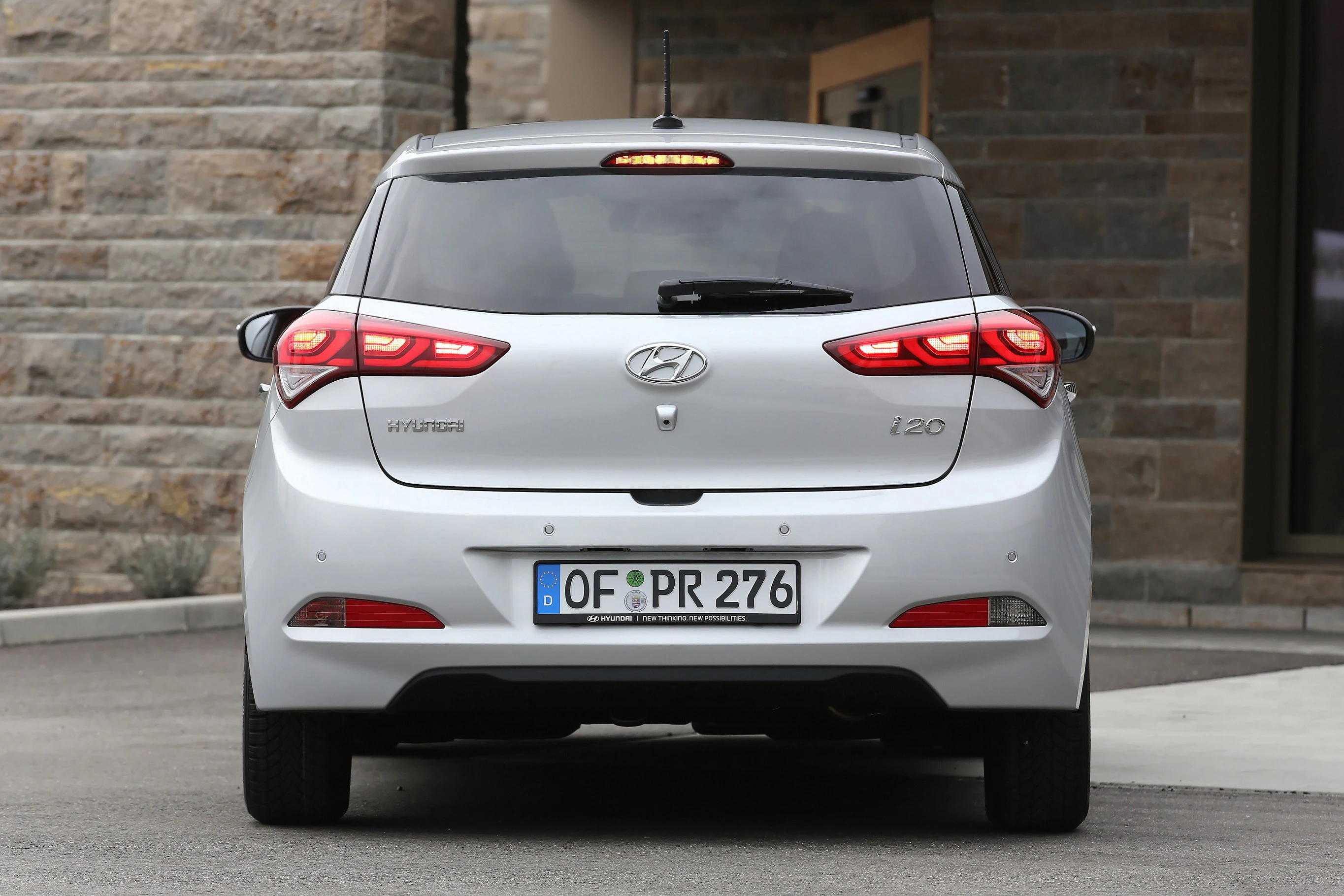 Rückansicht eines silbernen Hyundai i20, geparkt vor einem Gebäude. Das Auto hat deutsche Kennzeichen und leuchtet die Bremslichter.