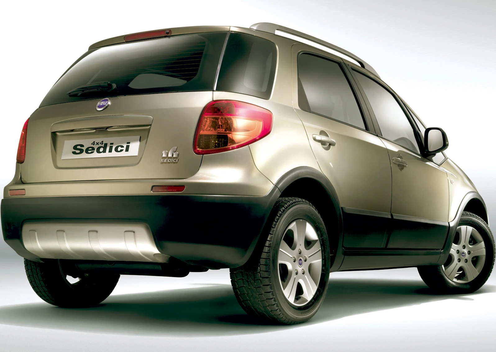 Fiat Sedici in Beige, Ansicht von hinten links, beleuchtete Rückleuchten, silberne Felgen, 4x4-Emblem, glänzender Lack, heller Hintergrund.