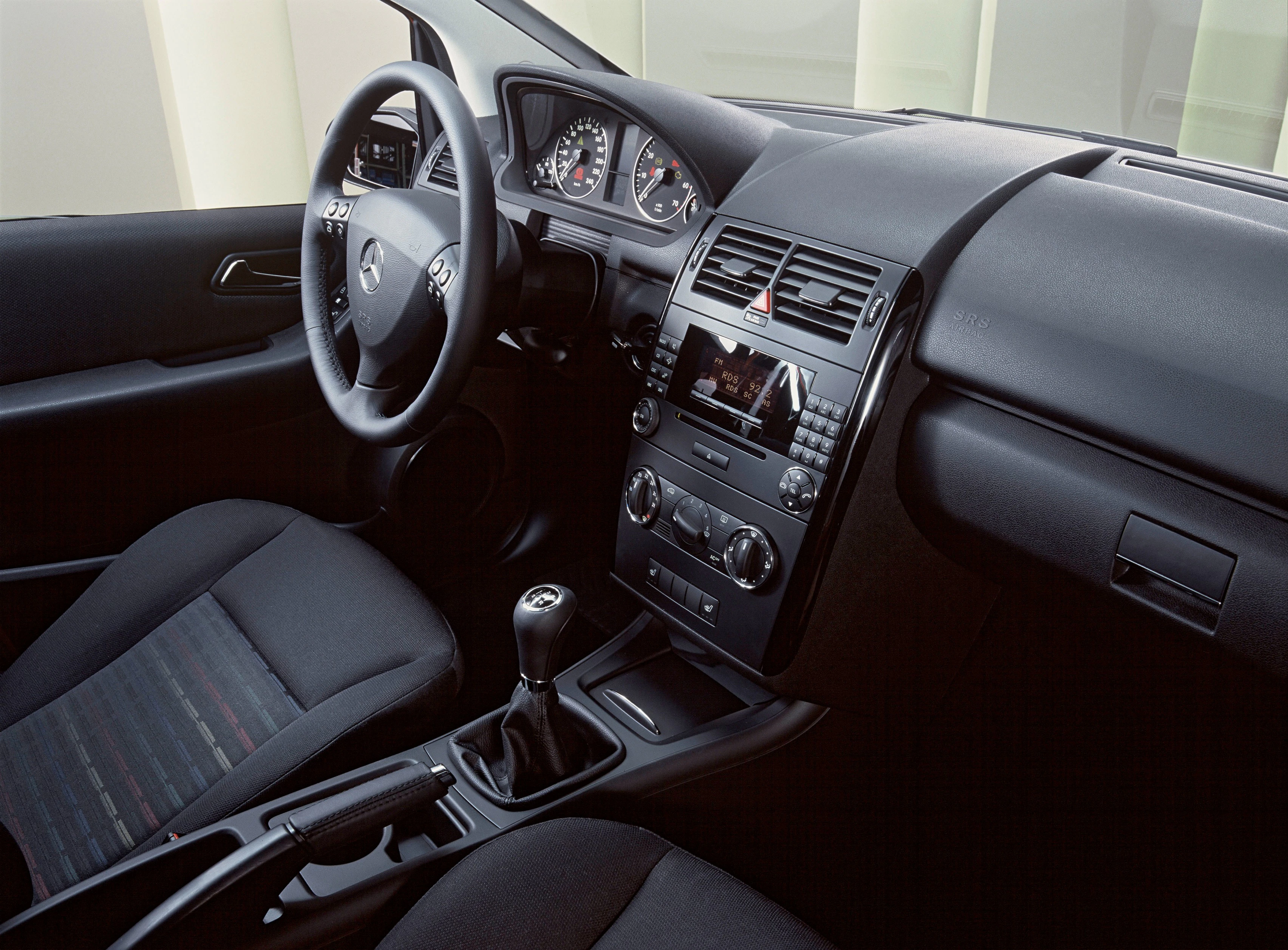 Innenraum eines Autos mit Lenkrad, Schalthebel, und Multimedia-System. Die Armaturen und Sitze sind in dunklen Farben gehalten.