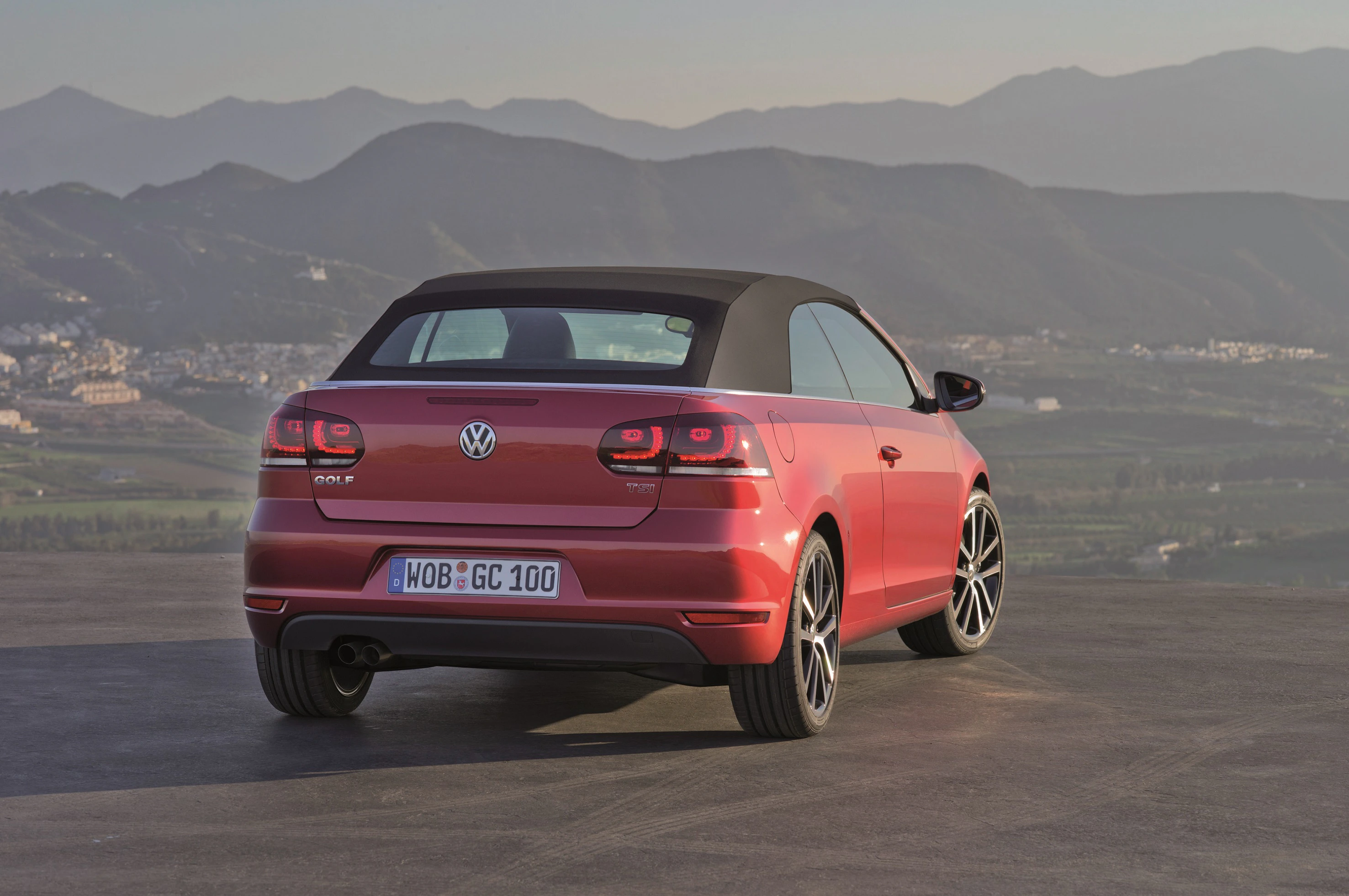Roter VW Golf Cabrio auf einem Parkplatz vor einer Berglandschaft, Heckansicht, bei Sonnenuntergang.
