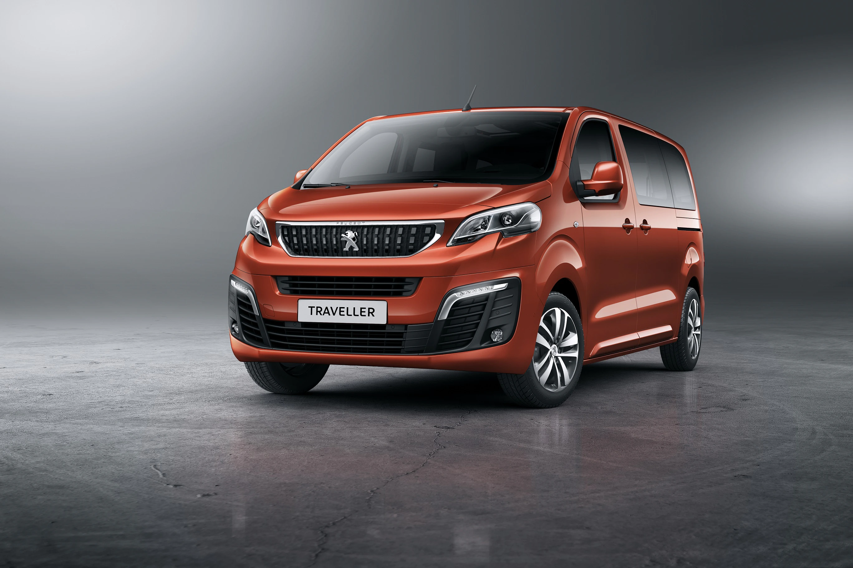 Roter Peugeot Traveller steht in einem grauen Studio, von vorne leicht versetzt. Modernes Design mit auffälligem Kühlergrill und LED-Scheinwerfern.