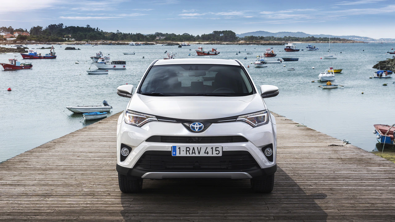 Weißer SUV auf Holzsteg am Meer, umgeben von kleinen Booten und blauem Himmel im Hintergrund.