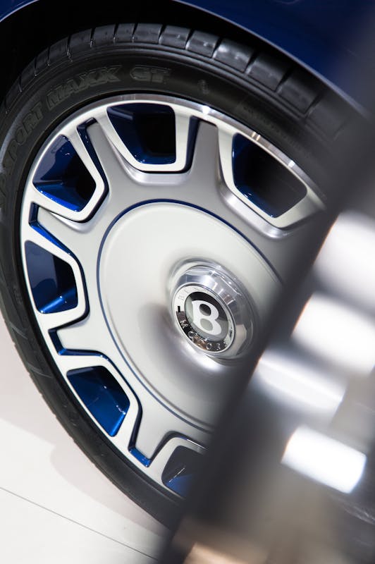 Nahaufnahme eines Autoreifens mit silbernen und blauen Details und einem markanten "B"-Logo in der Mitte der Felge.