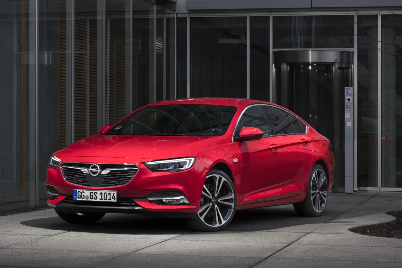 Roter Opel Insignia Grand Sport vor einem modernen Gebäude mit Glasfront geparkt. Elegantes Design und sportliche Linien.