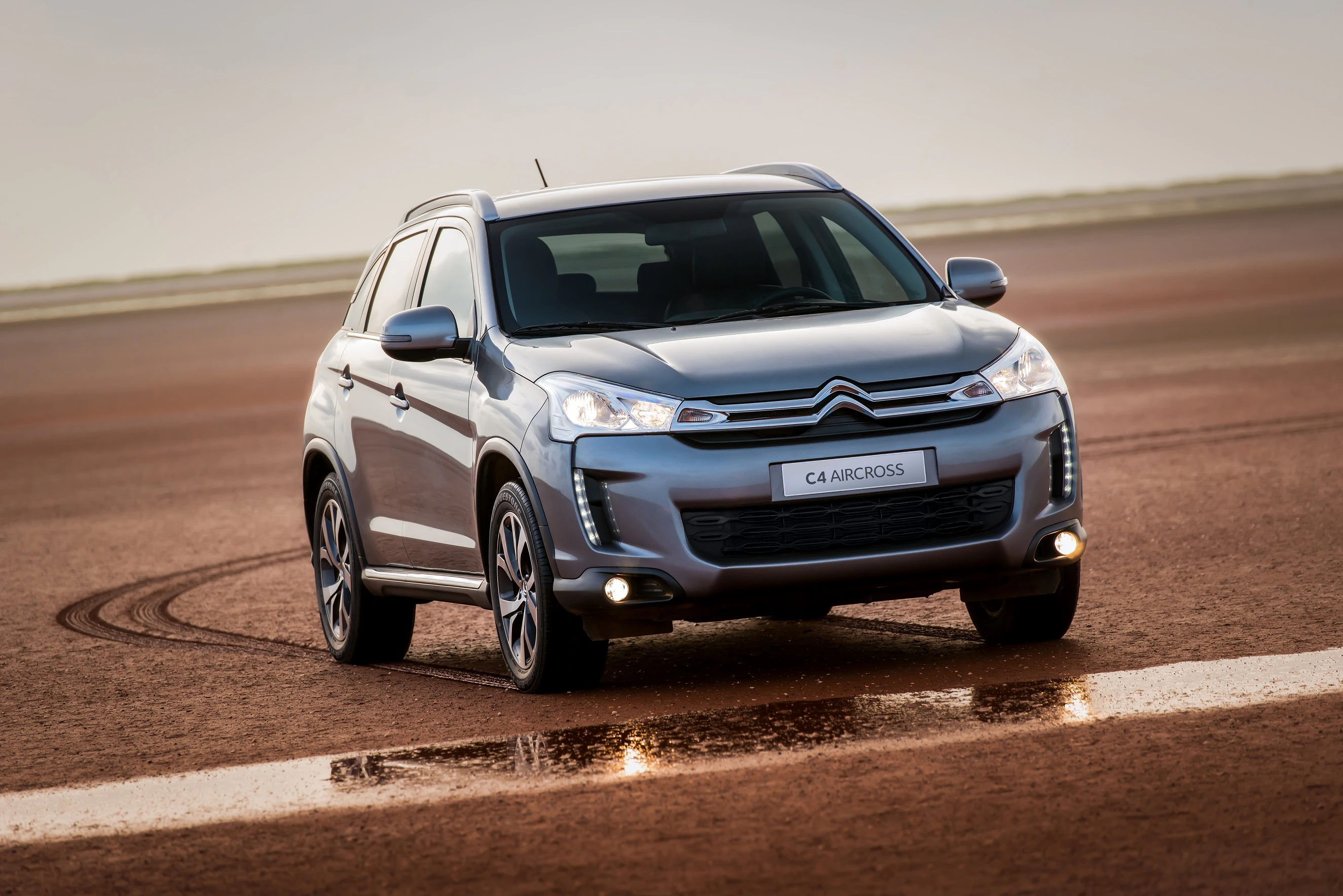 Silberner Citroën C4 Aircross parkt auf einer weiten, braunen Fläche im Freien.