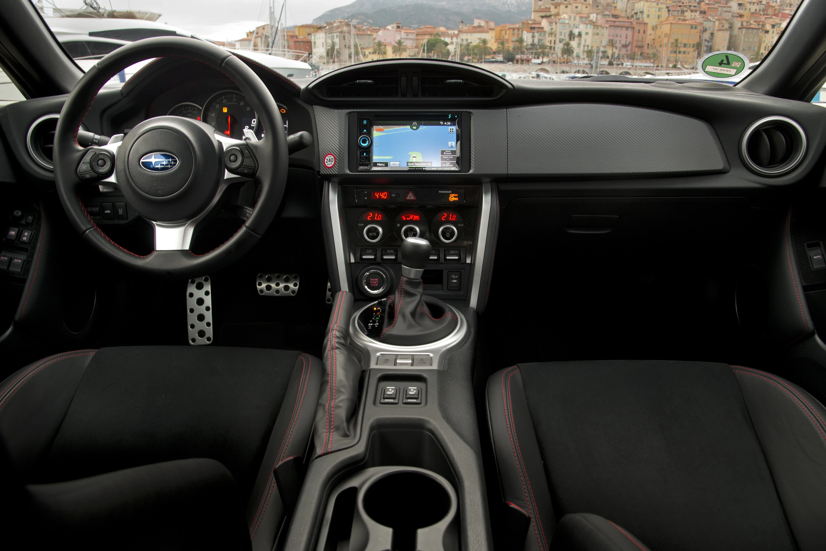 Innenraum eines sportlichen Autos mit schwarzem Interieur, zentraler Touchscreen, Tachometer, Schaltknüppel und Lenkrad mit Subaru-Logo.
