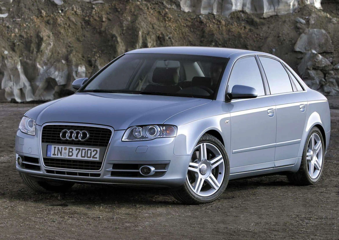 Silberner Audi Limousine geparkt auf einem unbefestigten Weg vor einer Felswand, seitliche Ansicht.